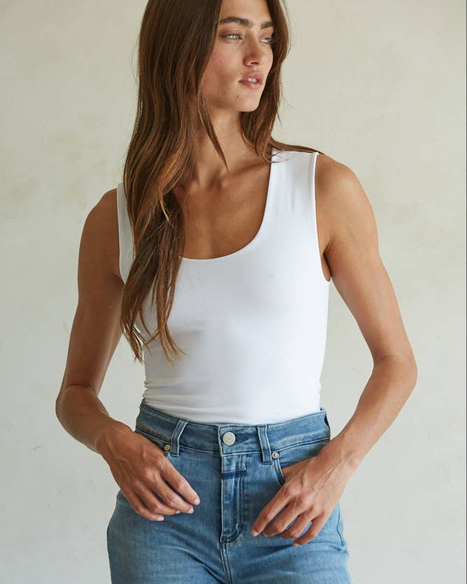 Woman wearing a white tank top and blue jeans against a plain background