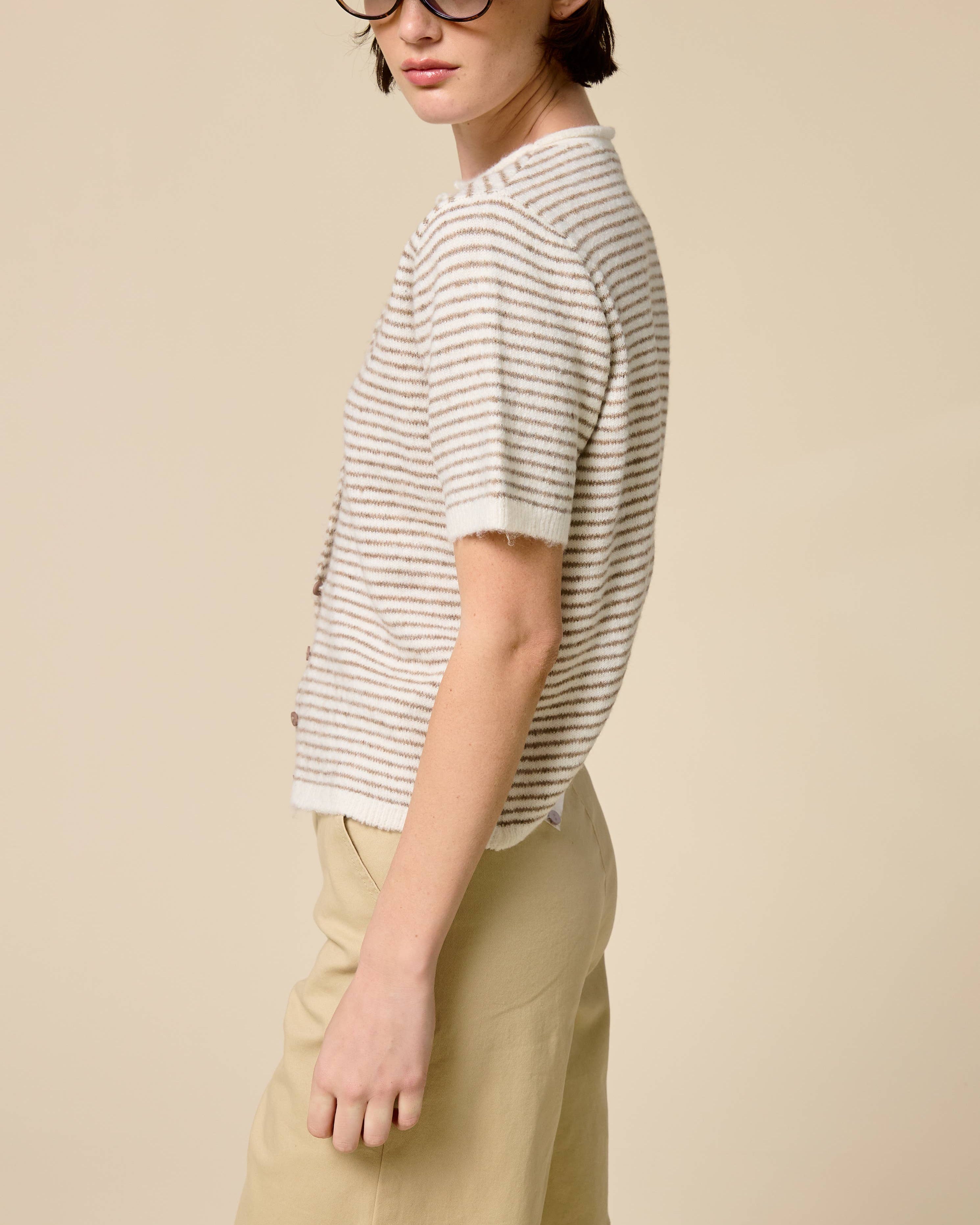 Person wearing a striped shirt, beige cap, and light-colored pants on a plain background