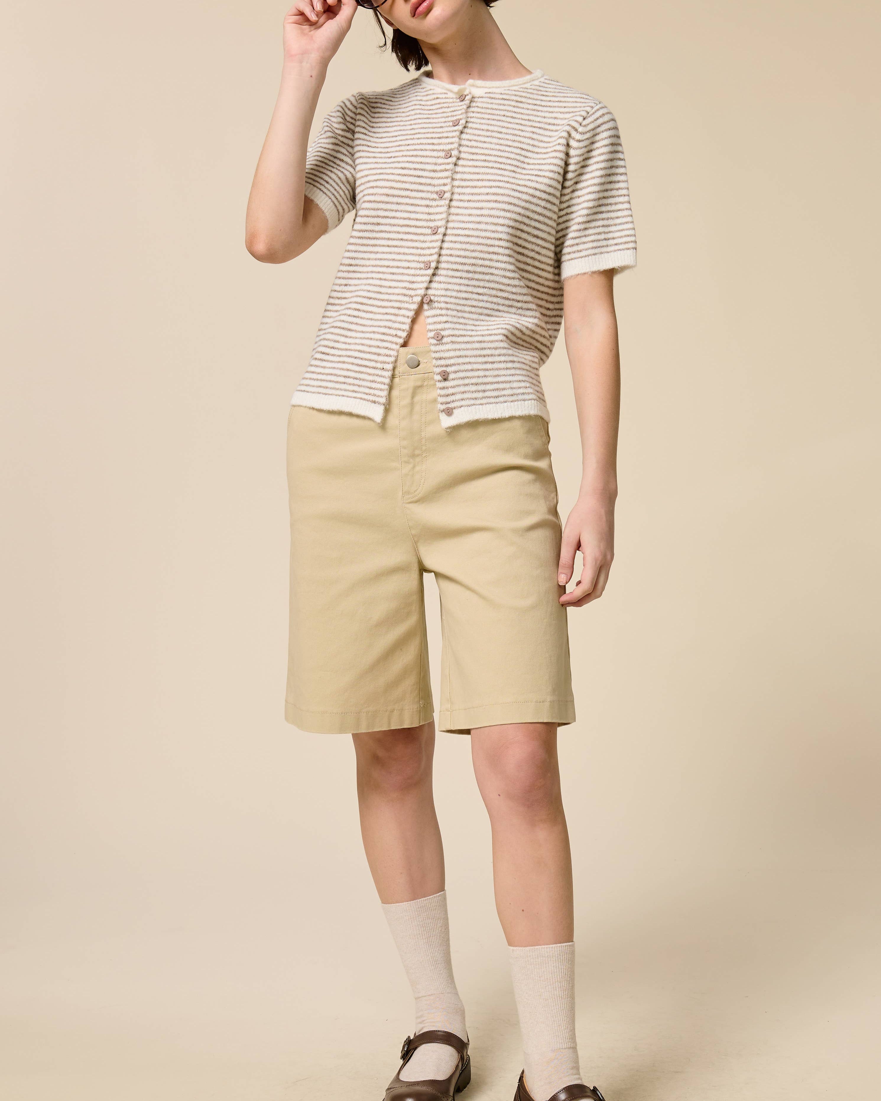 Person wearing a striped shirt, beige shorts, and a hat on a beige background