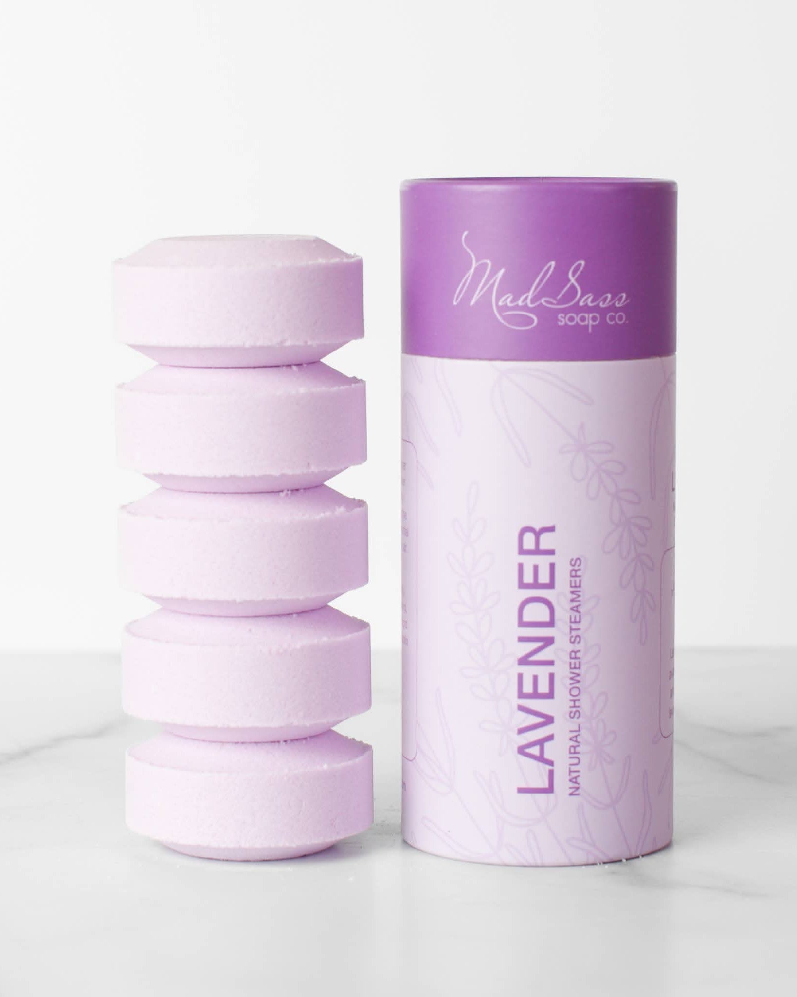 Stacked purple lavender shower steamer tablets next to packaging