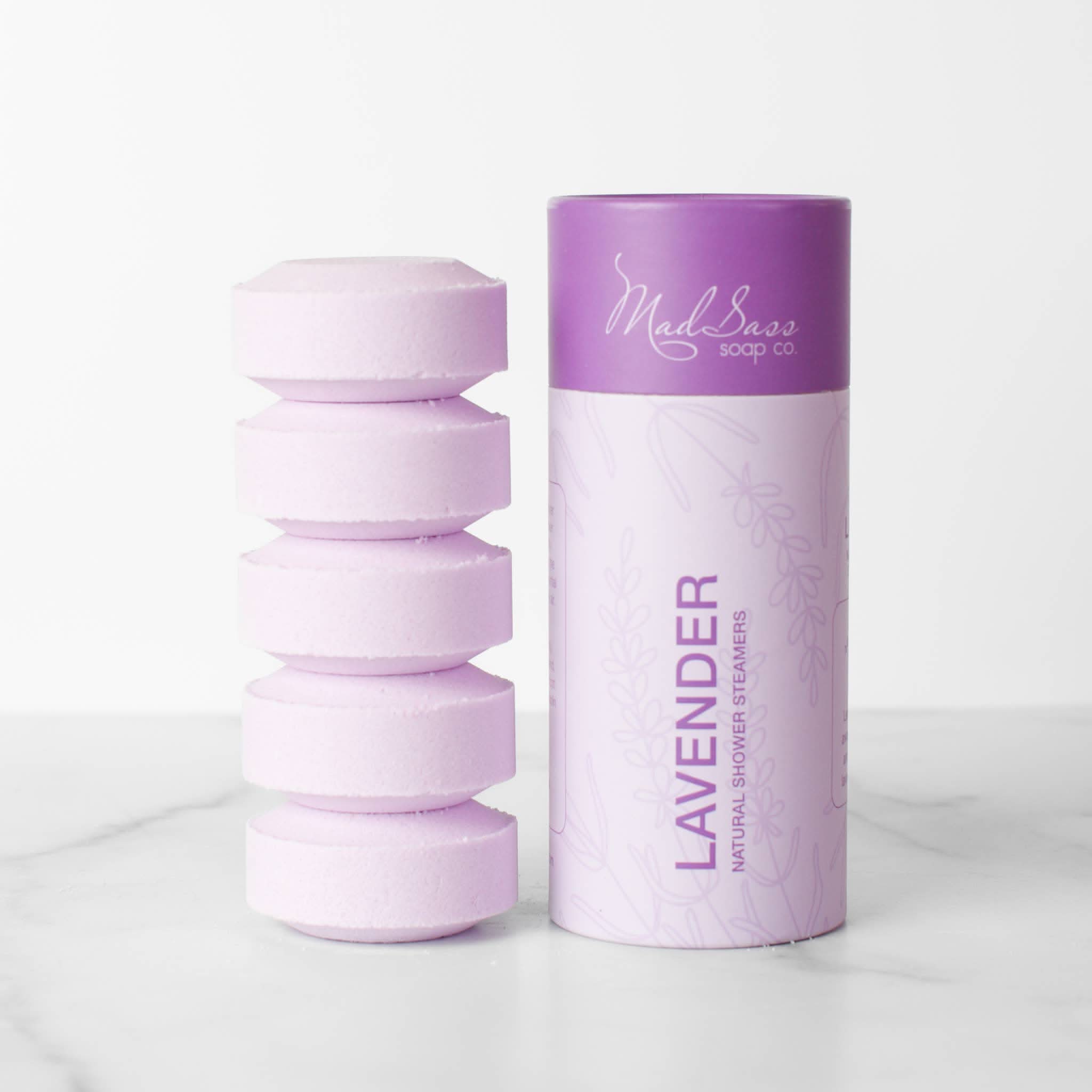 Stacked purple lavender shower steamer tablets next to packaging