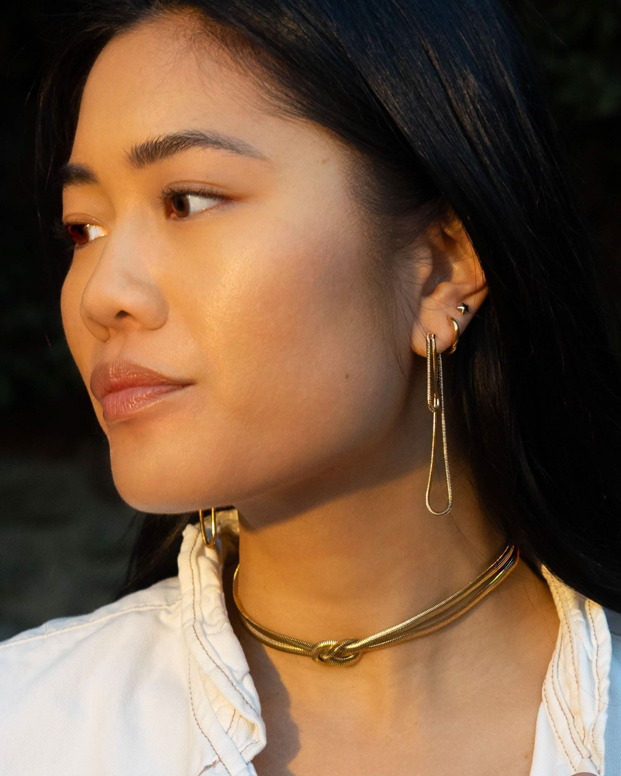 Woman wearing long abstract loop earrings and gold figure eight knot herringbone choker necklace