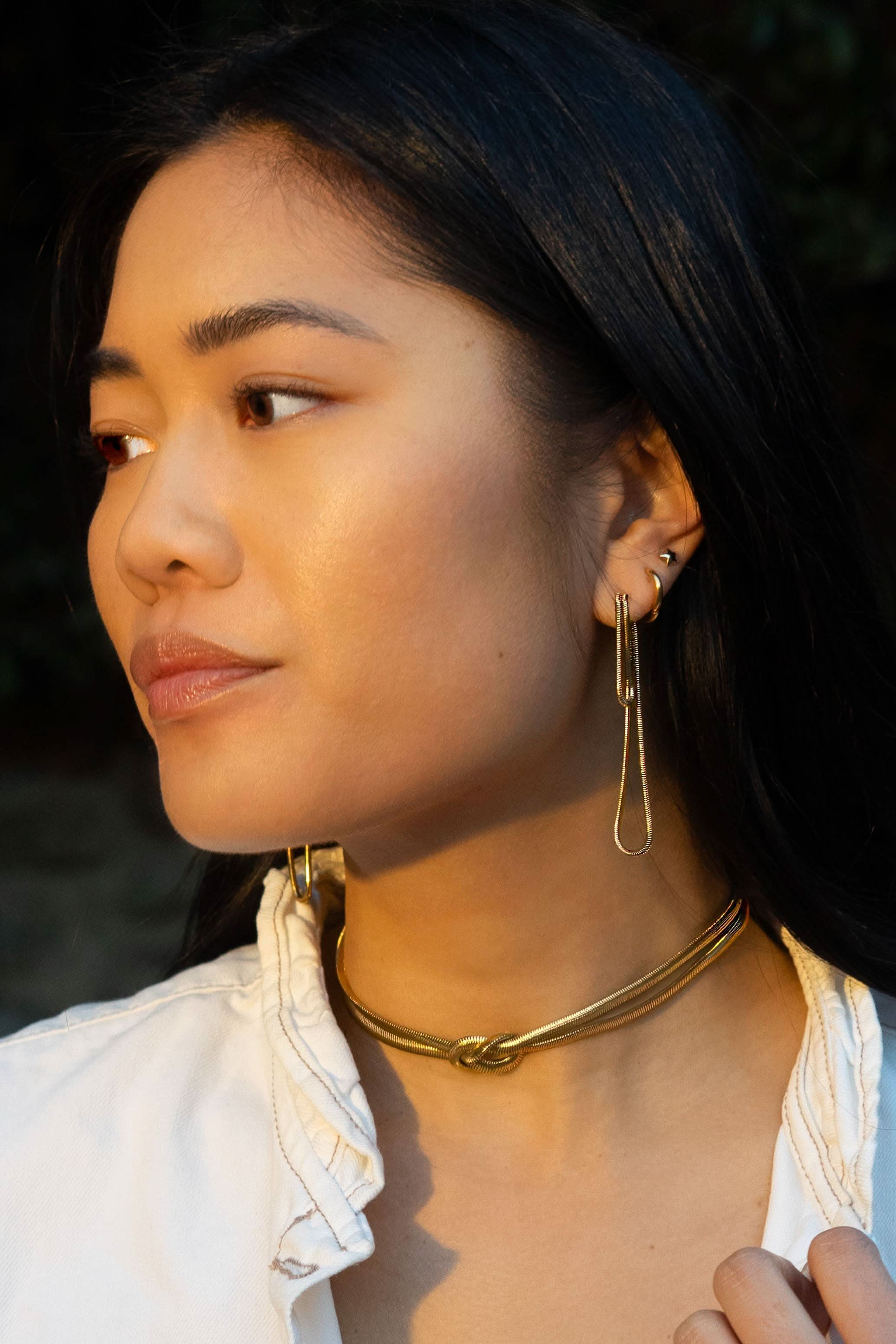 Woman wearing long abstract loop earrings and gold figure eight knot herringbone choker necklace