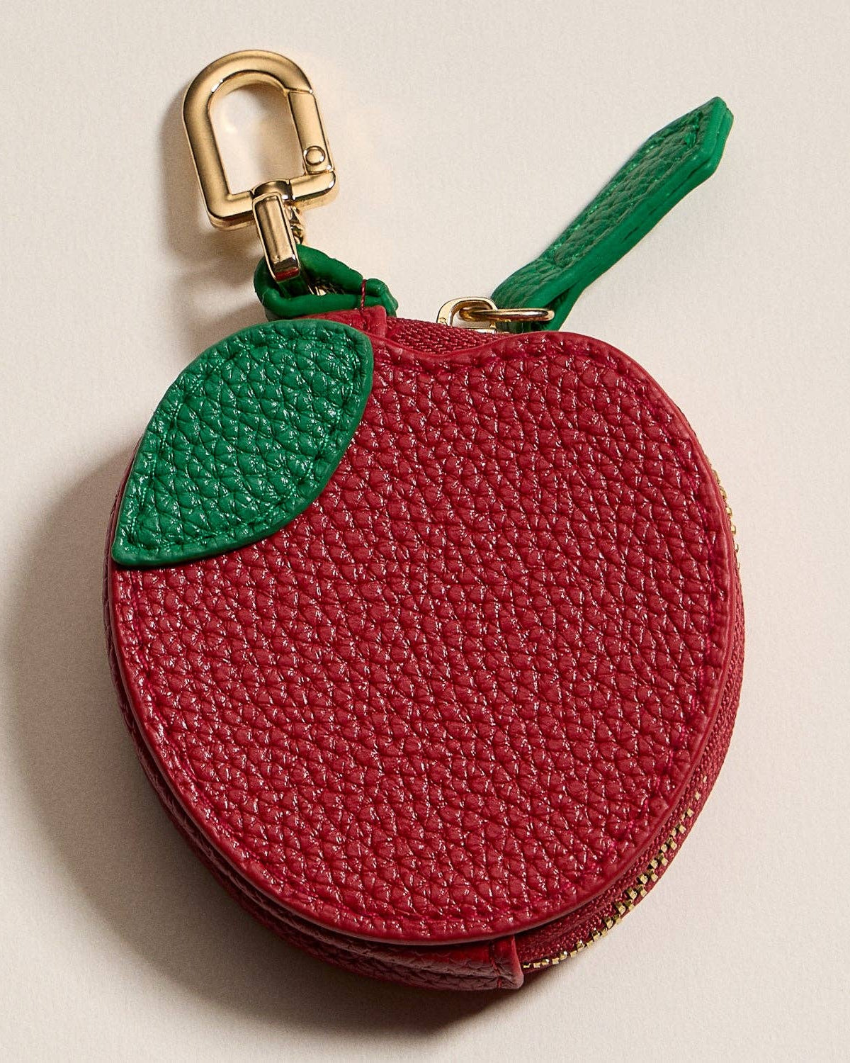 Red apple-shaped keychain purse with a gold clasp on a beige background
