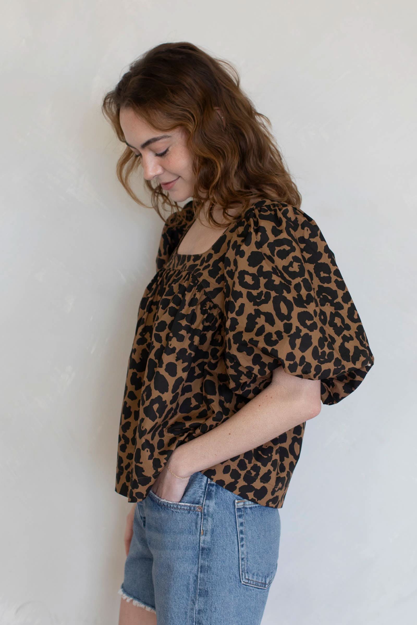 Red haired woman wearing leopard puff sleeve top with blue jean shorts