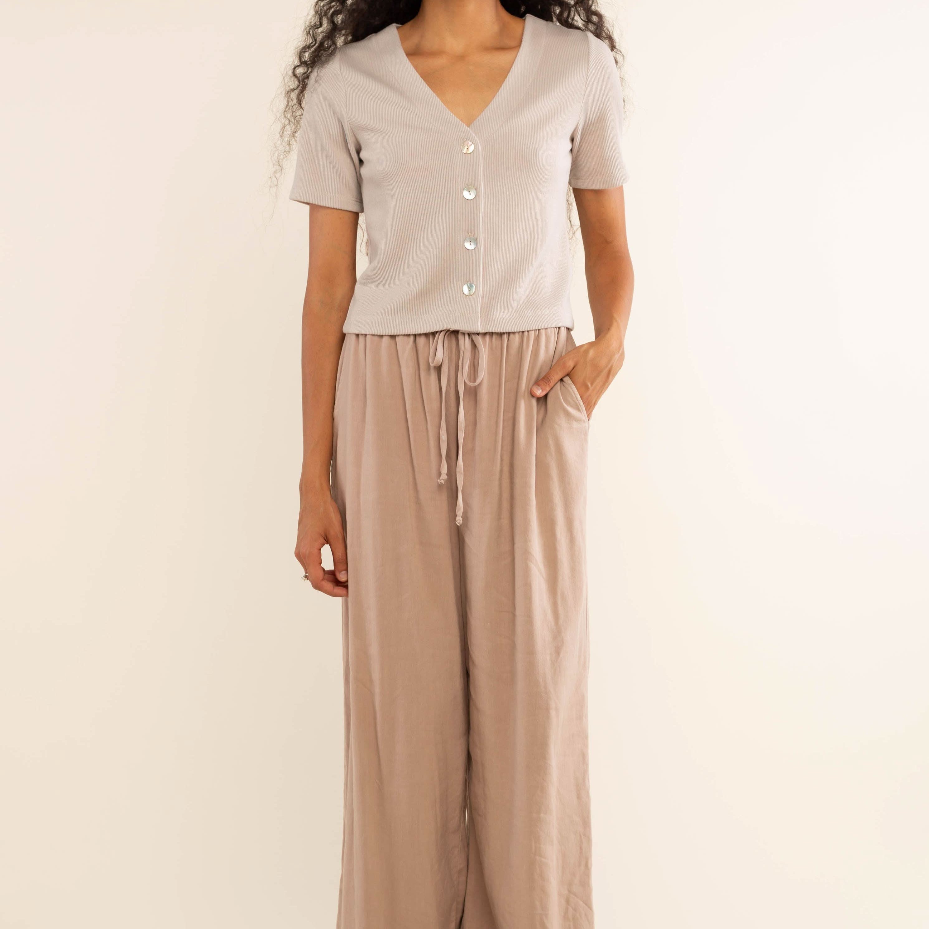 Woman wearing oat colored, ribbed, button down, short sleeve blouse top and beige pants