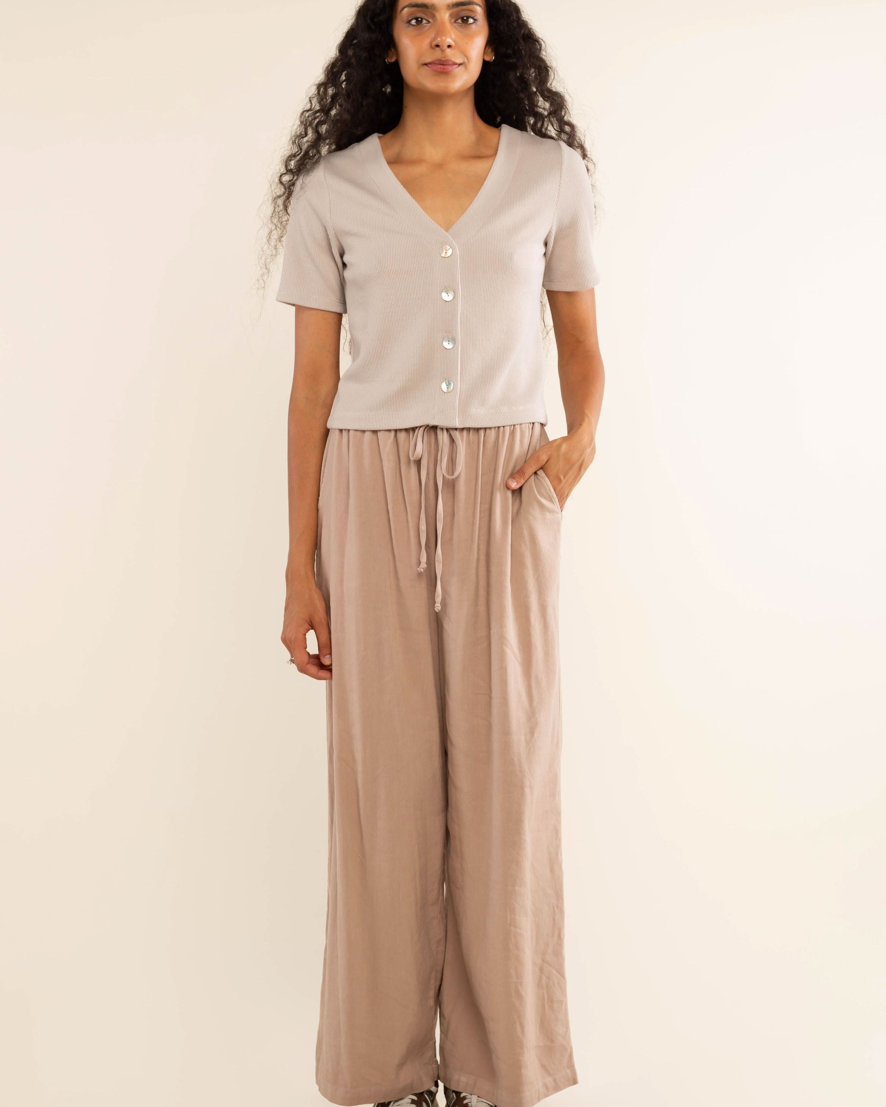 Woman wearing oat colored, ribbed, button down, short sleeve blouse top and beige pants