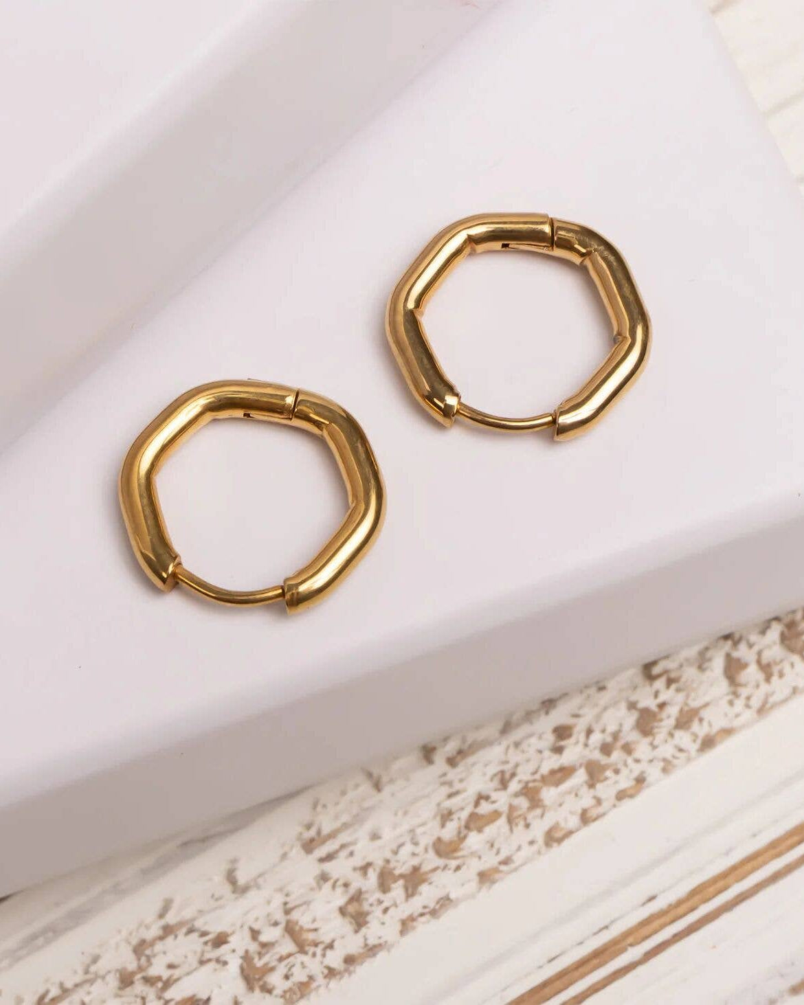 Gold hoop earrings on a textured white surface