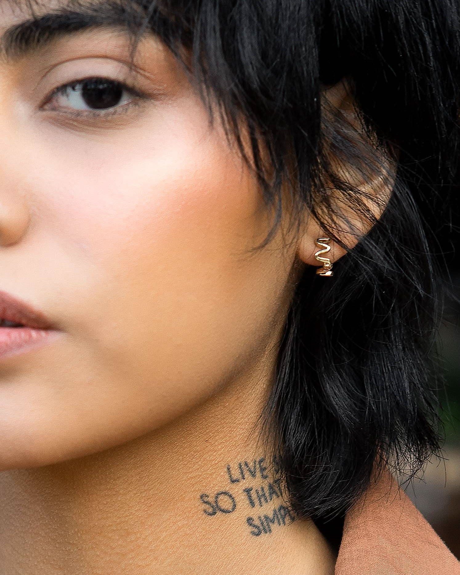 model wearing wiggly small gold huggie style hoop earrings