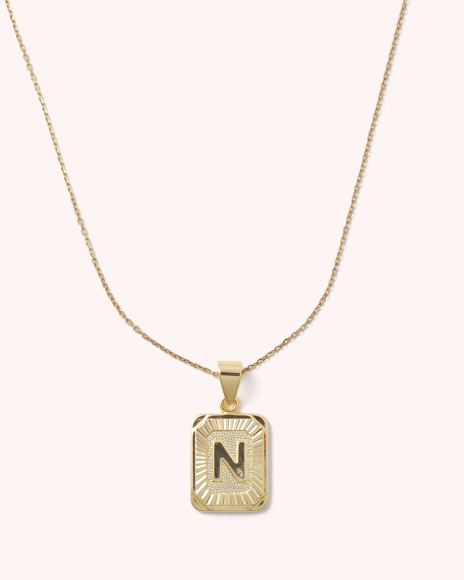 Letter N tarnish free gold initial charm necklace behind a blank background.