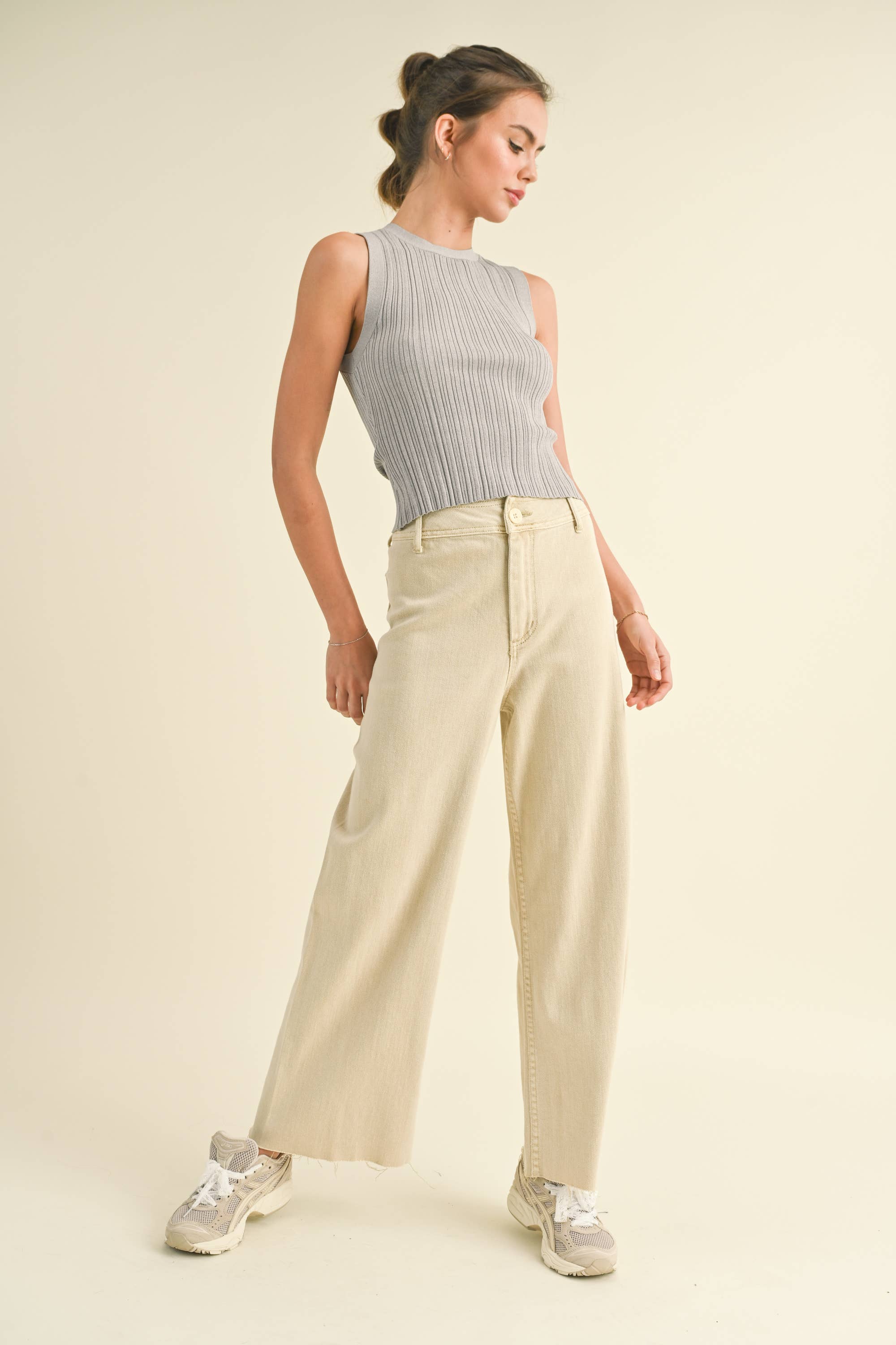 Woman wearing a sleeveless ribbed top and beige pants on a plain background