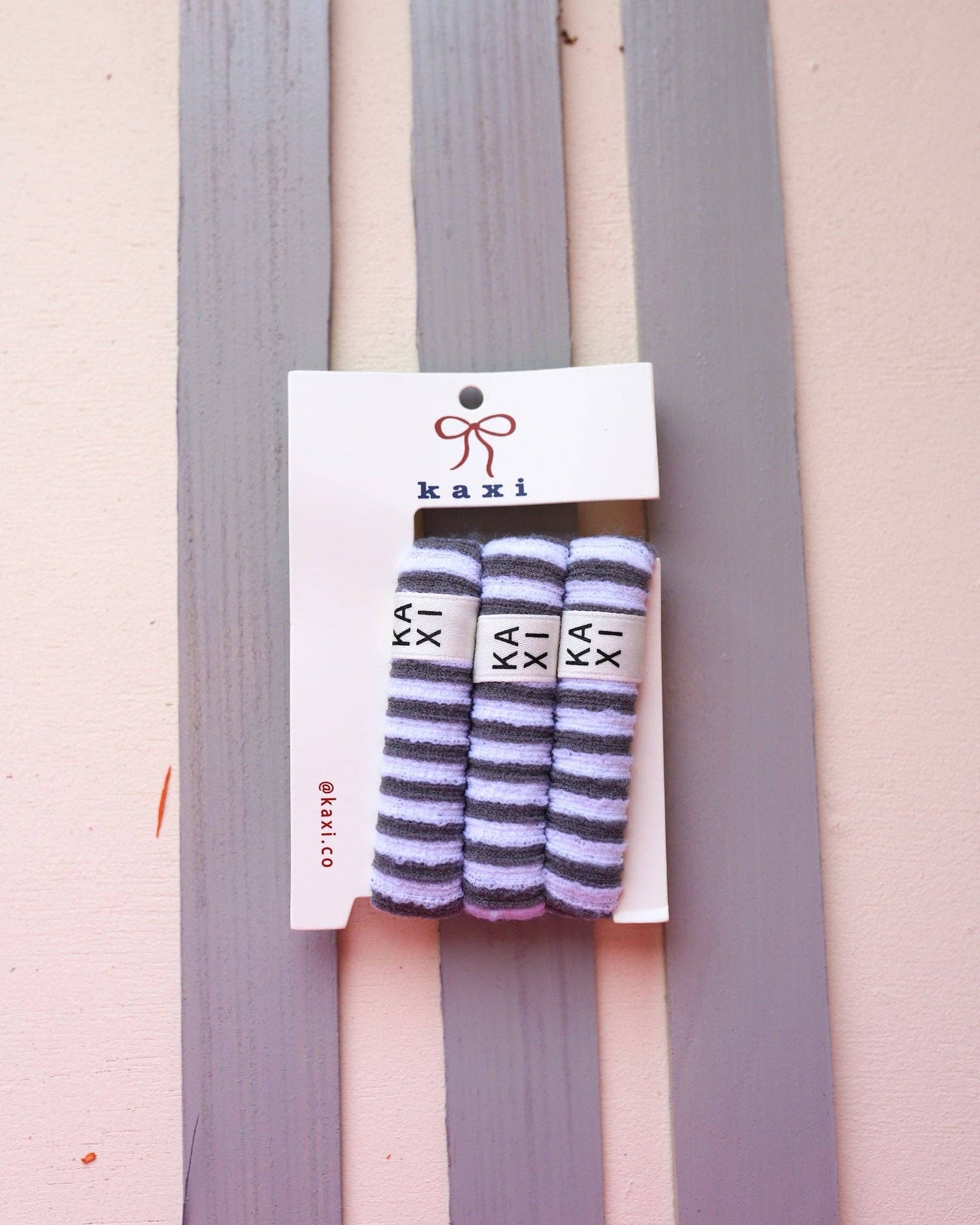 Striped socks on a pink and gray striped background with 'kaxi' branding.