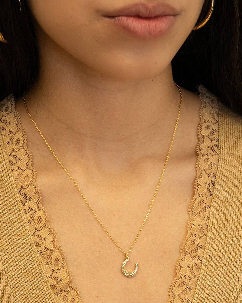 Close-up of a person wearing a gold necklace with a crescent moon pendant.