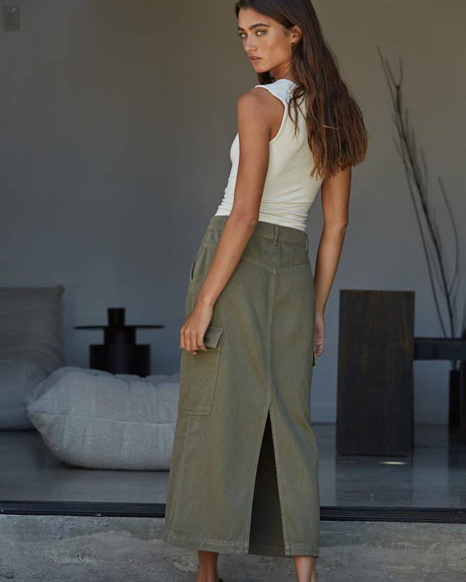 Woman wearing a white tank top and green pants standing in a modern indoor setting.