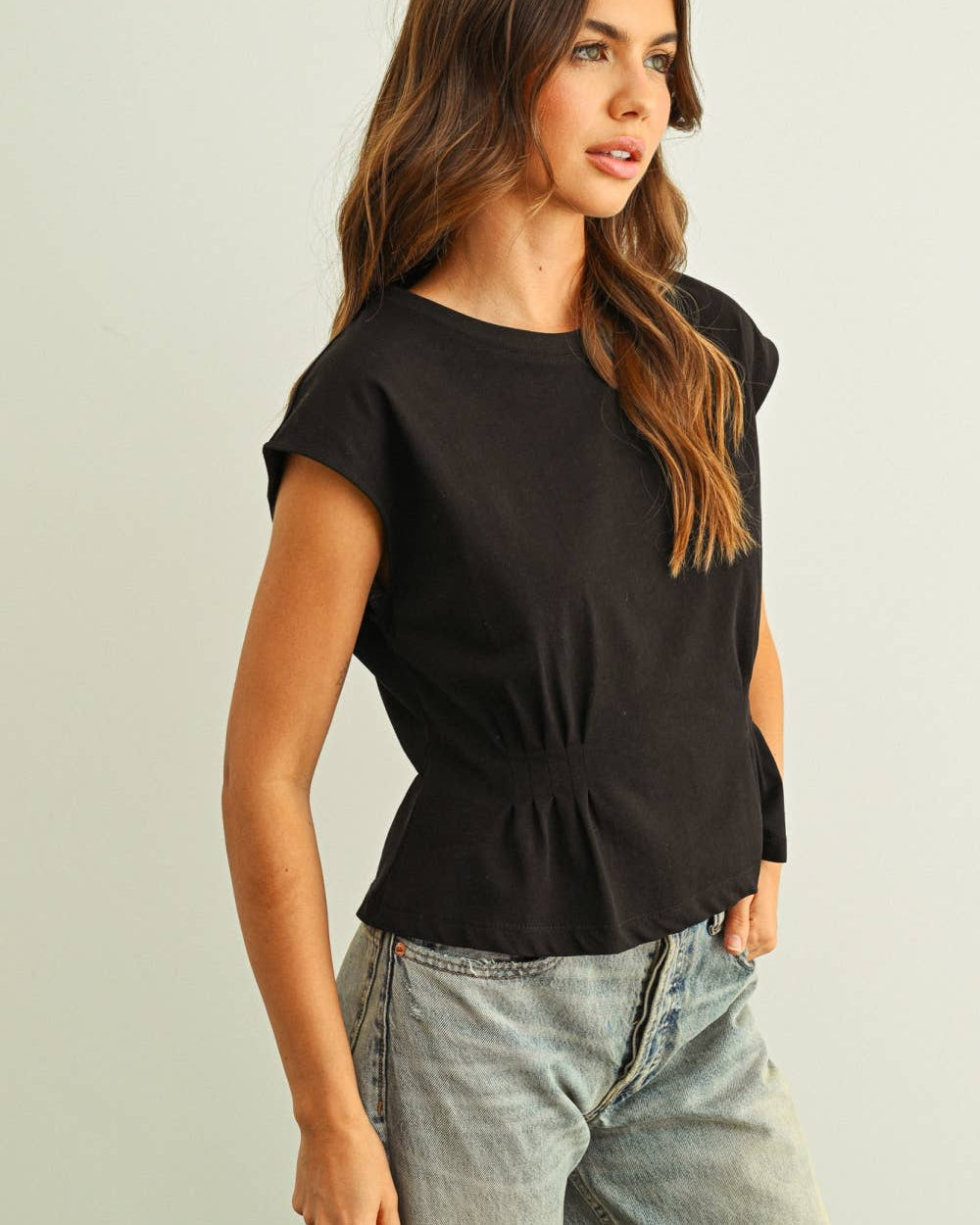 Woman wearing a black top and light blue jeans against a plain background