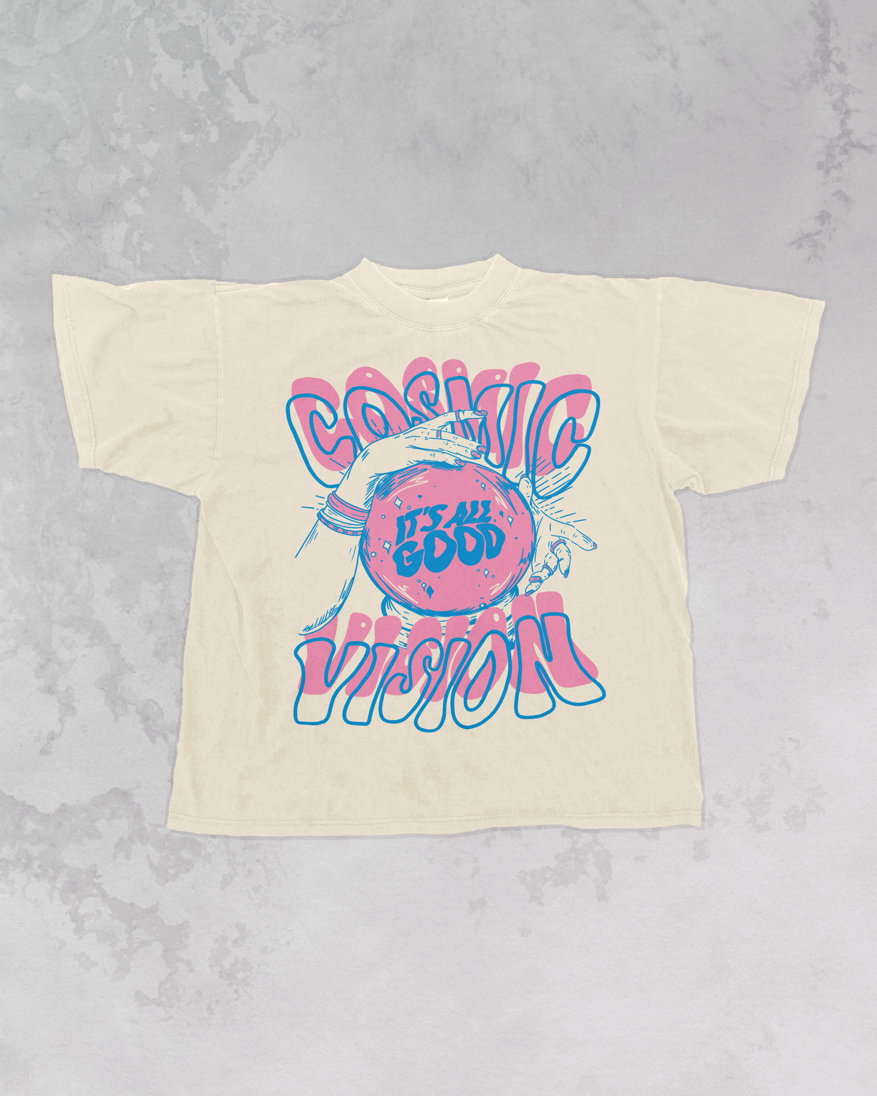 “It’s all good cosmic vision” pink and blue retro t-shirt laying on a gray marbled background