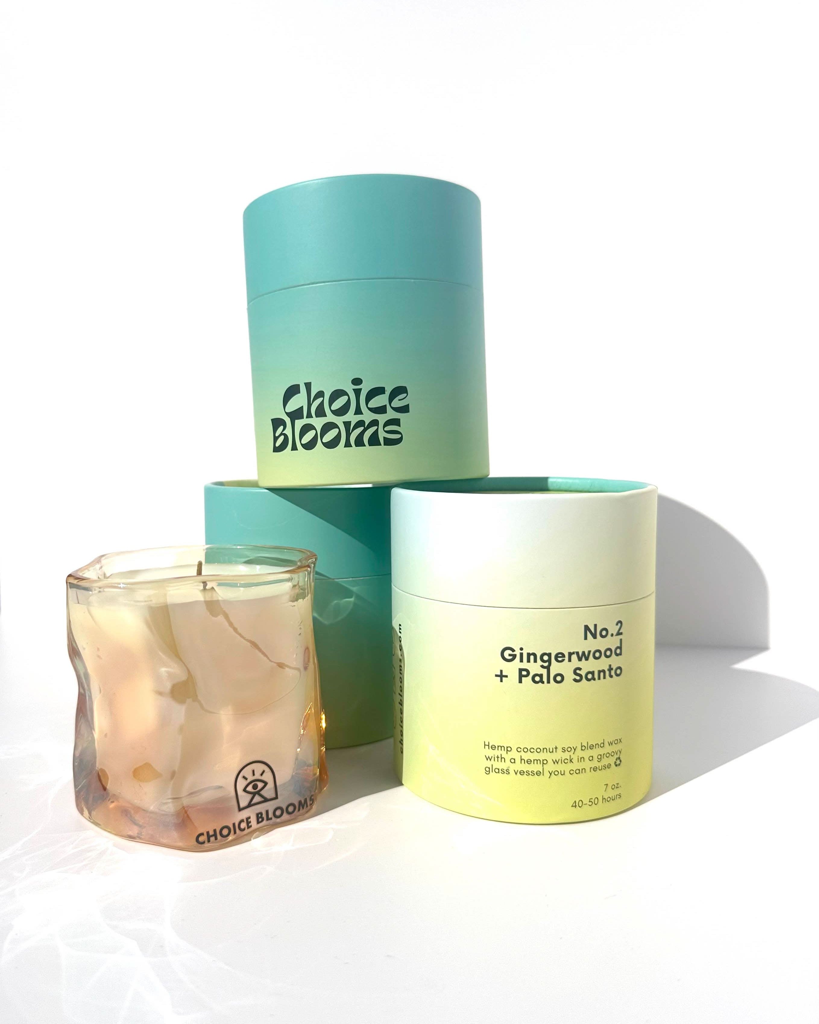One candle in tinted pink wavy glass container next to three Aqua and green candle packaging containers