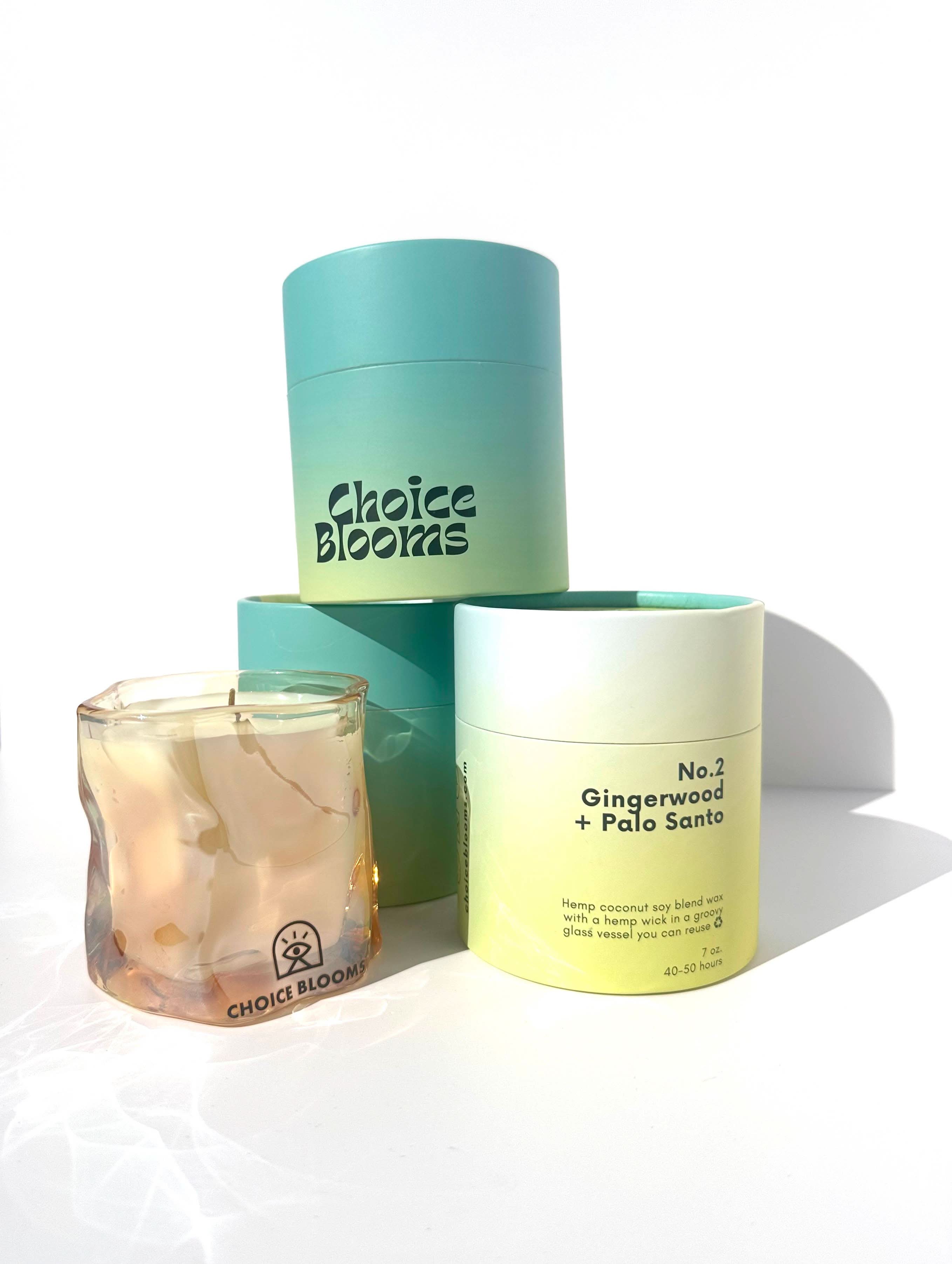 One candle in tinted pink wavy glass container next to three Aqua and green candle packaging containers