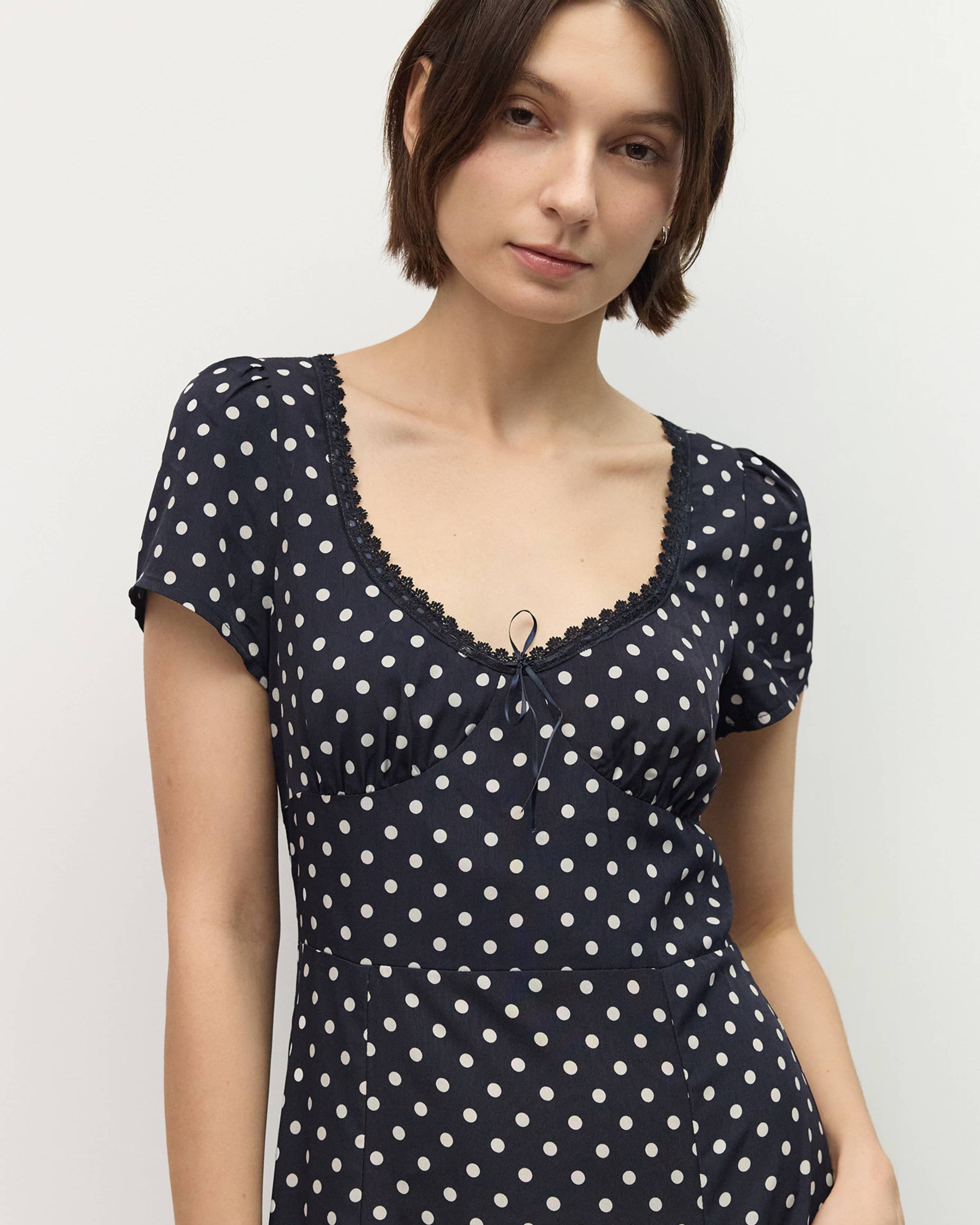 Woman wearing a navy blue dress with white polka dots against a plain background