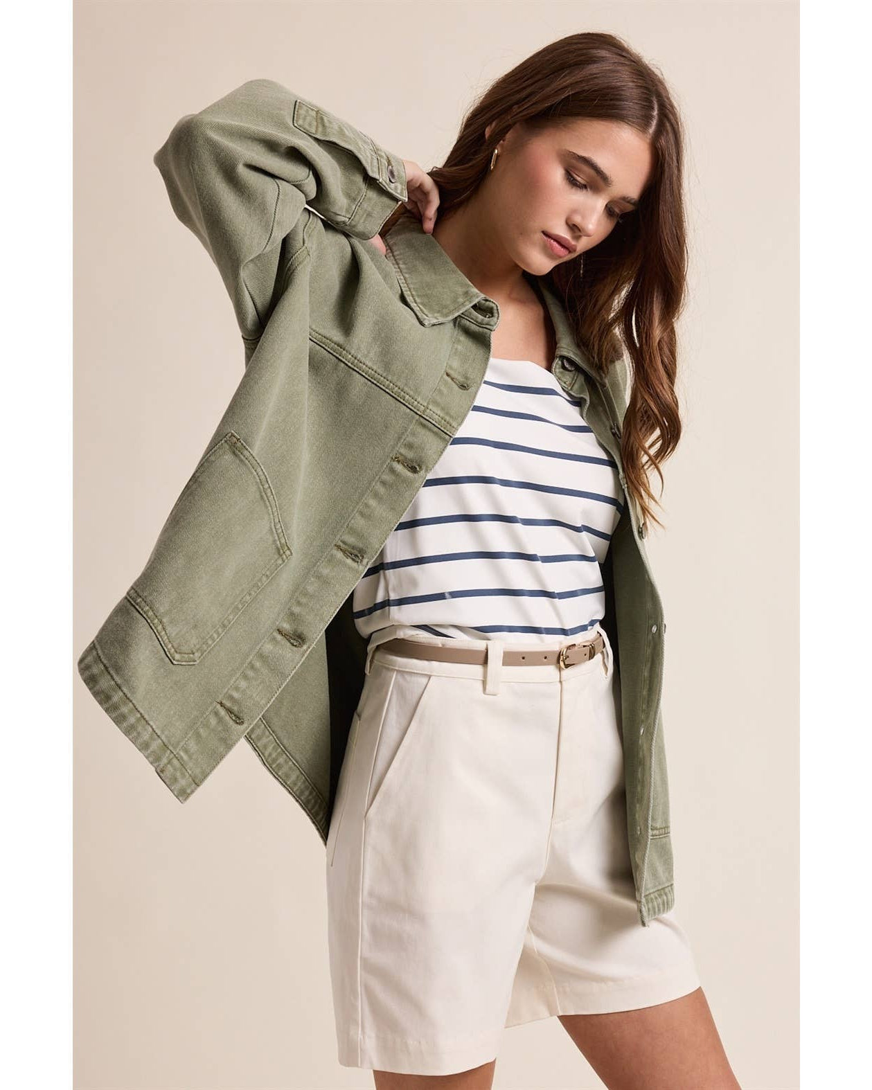 Woman wearing a green jacket, striped shirt, and white shorts on a beige background