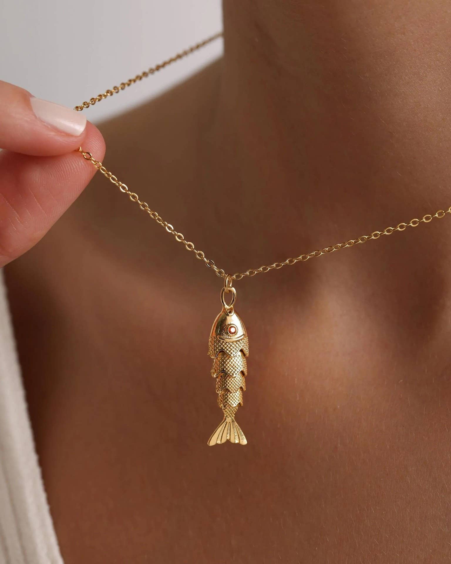 Gold fish pendant necklace being held by a hand against a neutral background