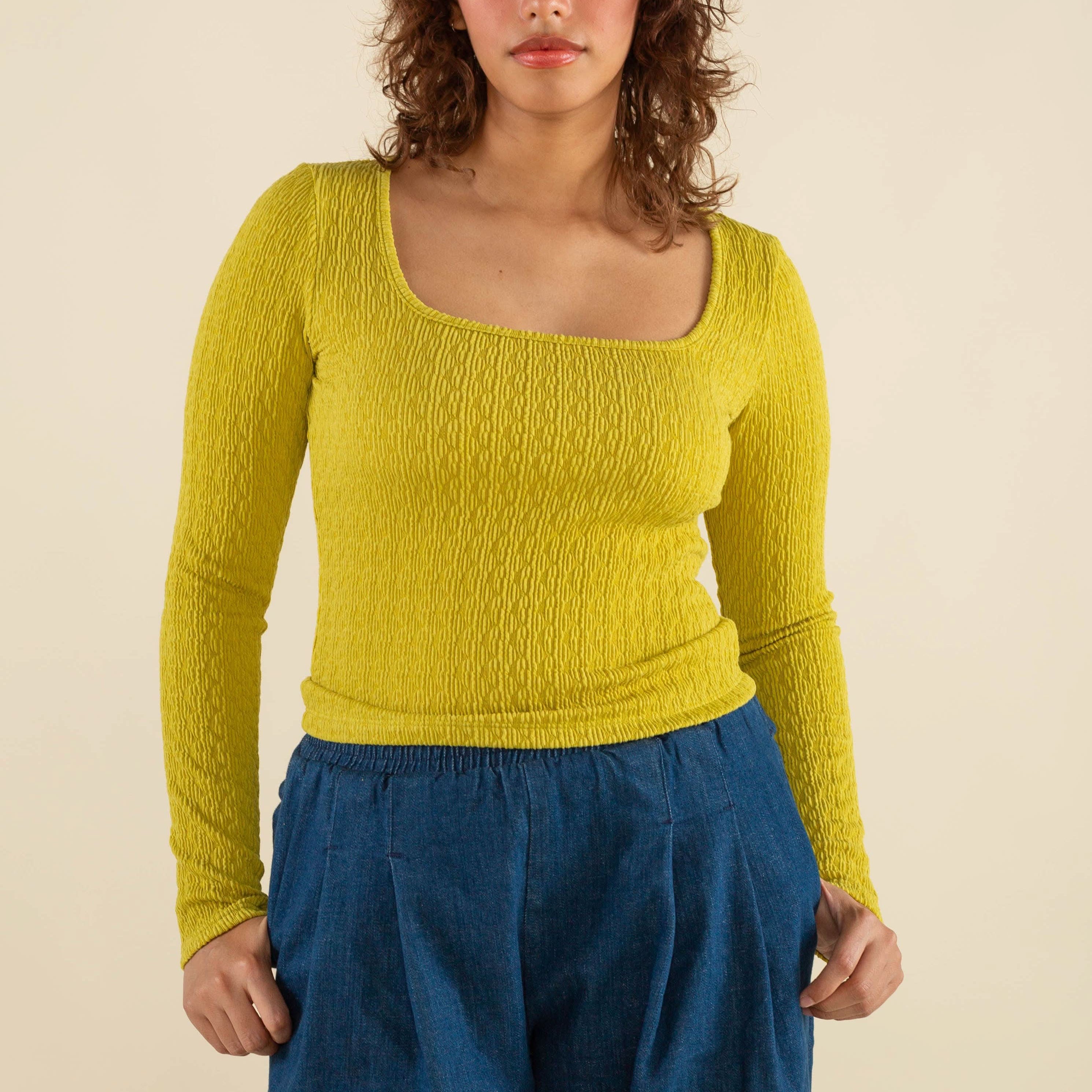 Woman wearing chartreuse, square neck line, textured, long sleeve top and jeans