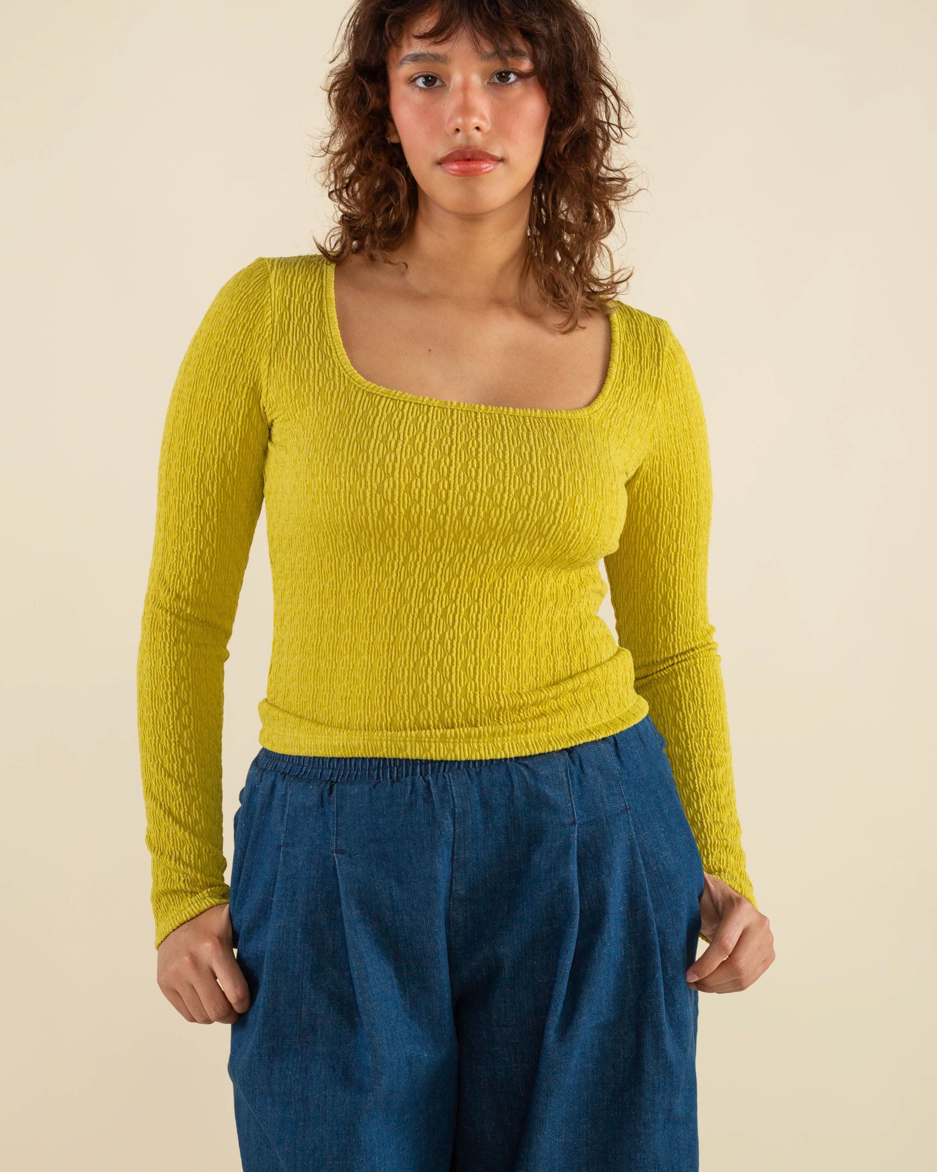 Woman wearing chartreuse, square neck line, textured, long sleeve top and jeans