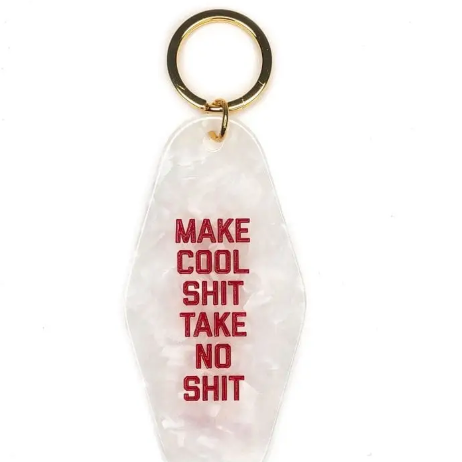 White marbled motel keychain that has red letters that say Make Cool Shit Take No Shit