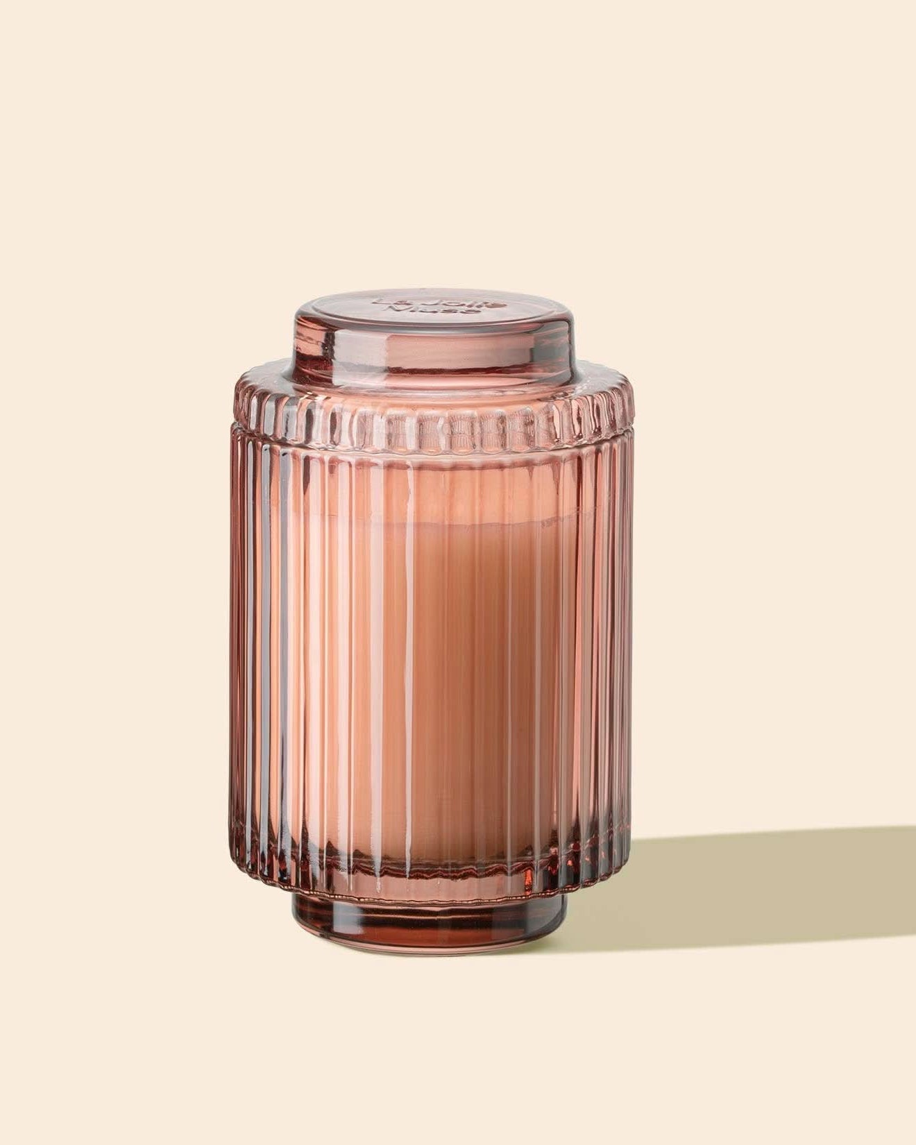 Pink glass candle jar with ribbed texture on a beige background