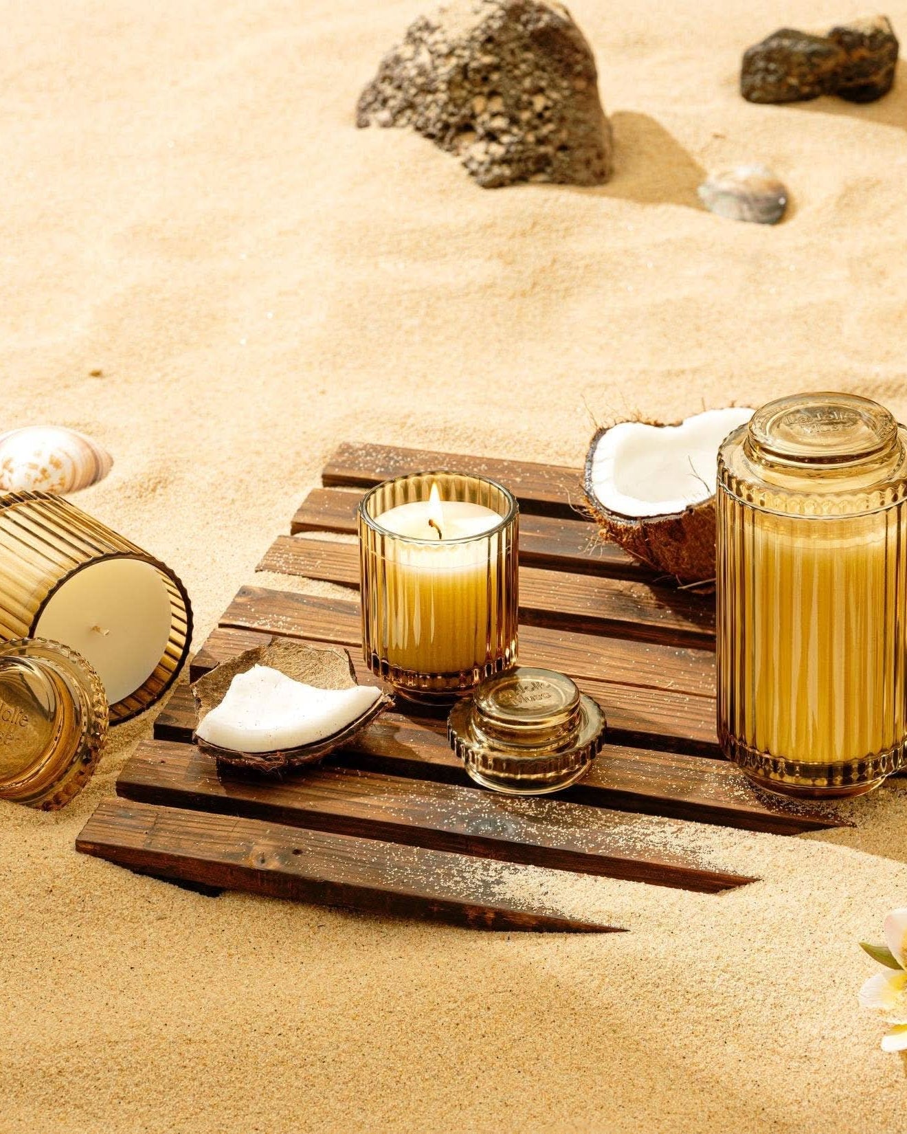 Candle holders and candles on a wooden board with seashells and flowers on sand