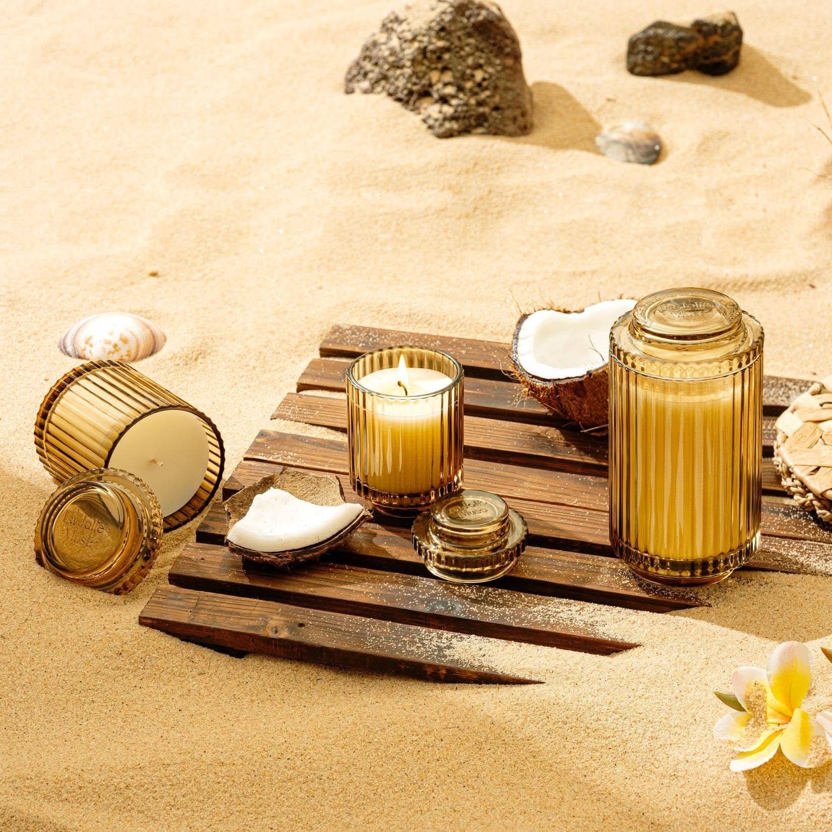 Candle holders and candles on a wooden board with seashells and flowers on sand