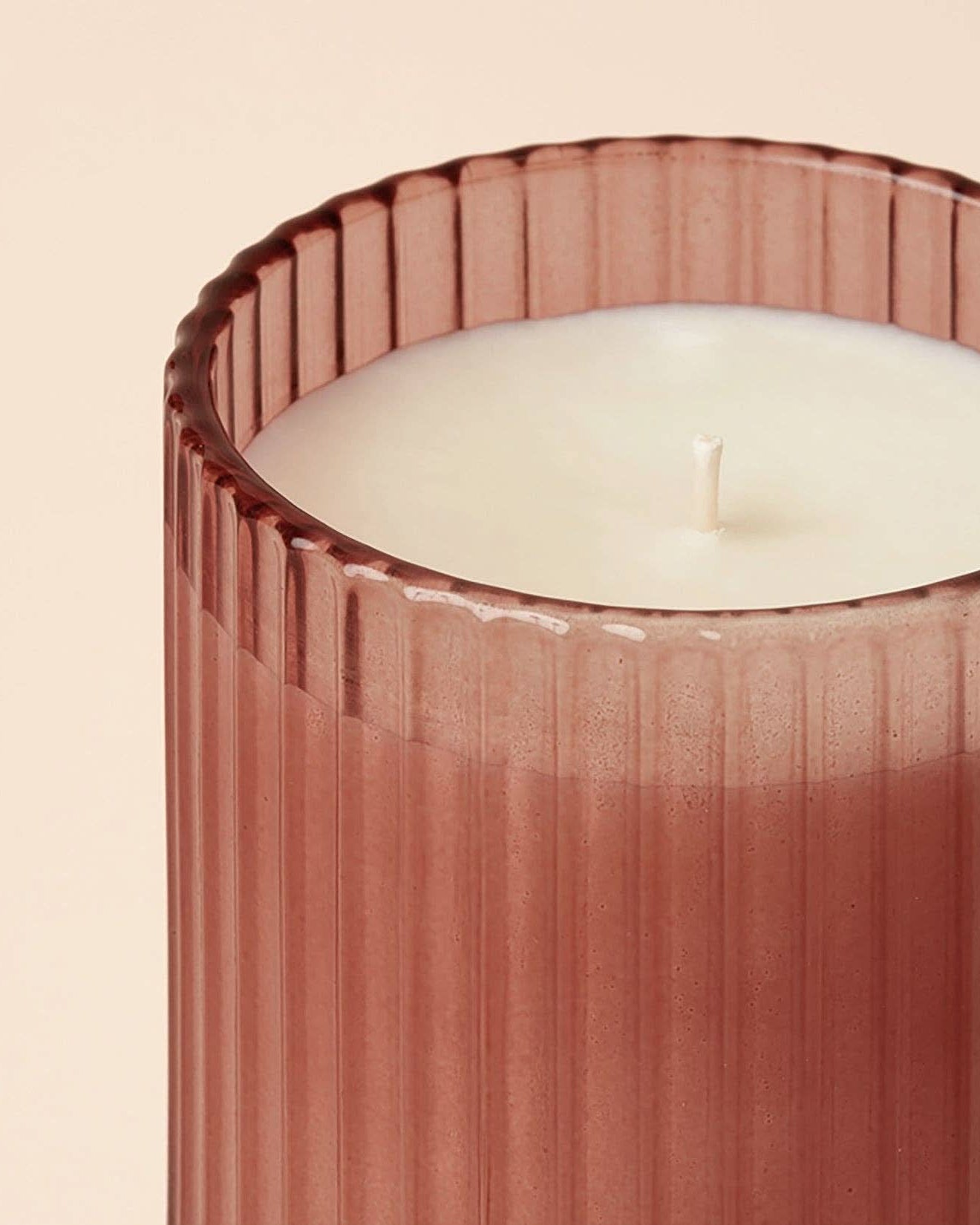 Candle in a ribbed pink holder on a beige background