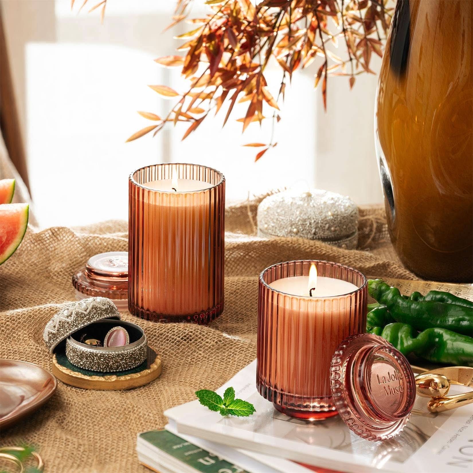 Decorative candles in brown glass containers on a table with books and a vase.