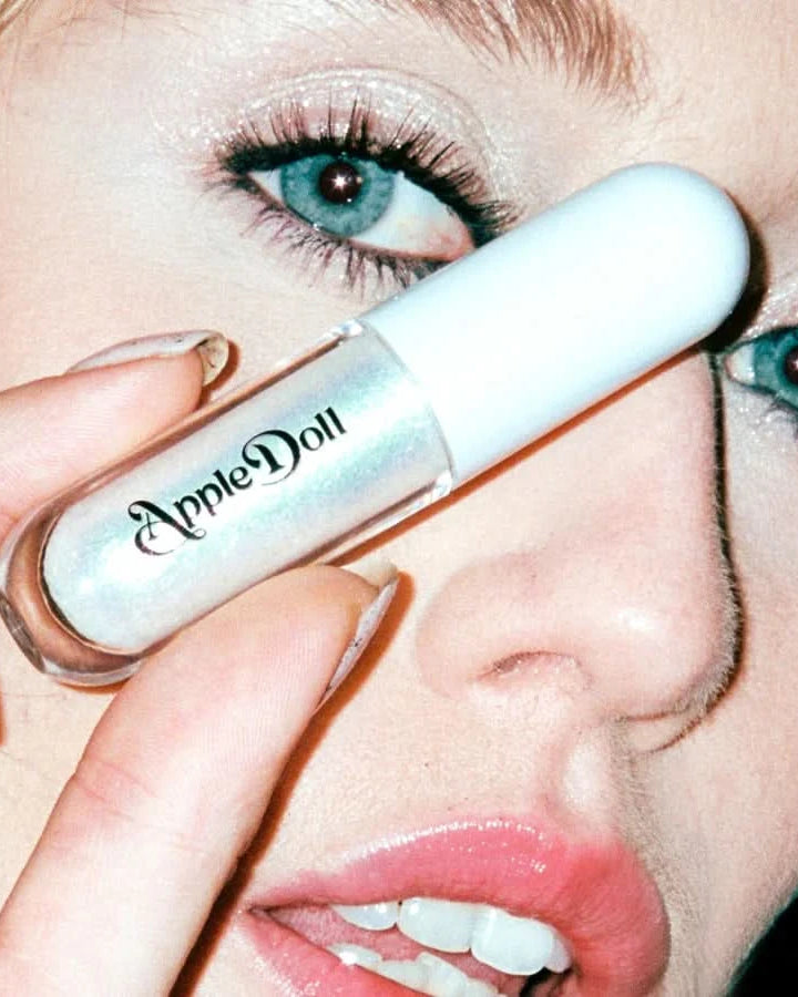Close-up of a model holding the AppleDoll Cosmic Aphrodite Crème Shadow tube over her face