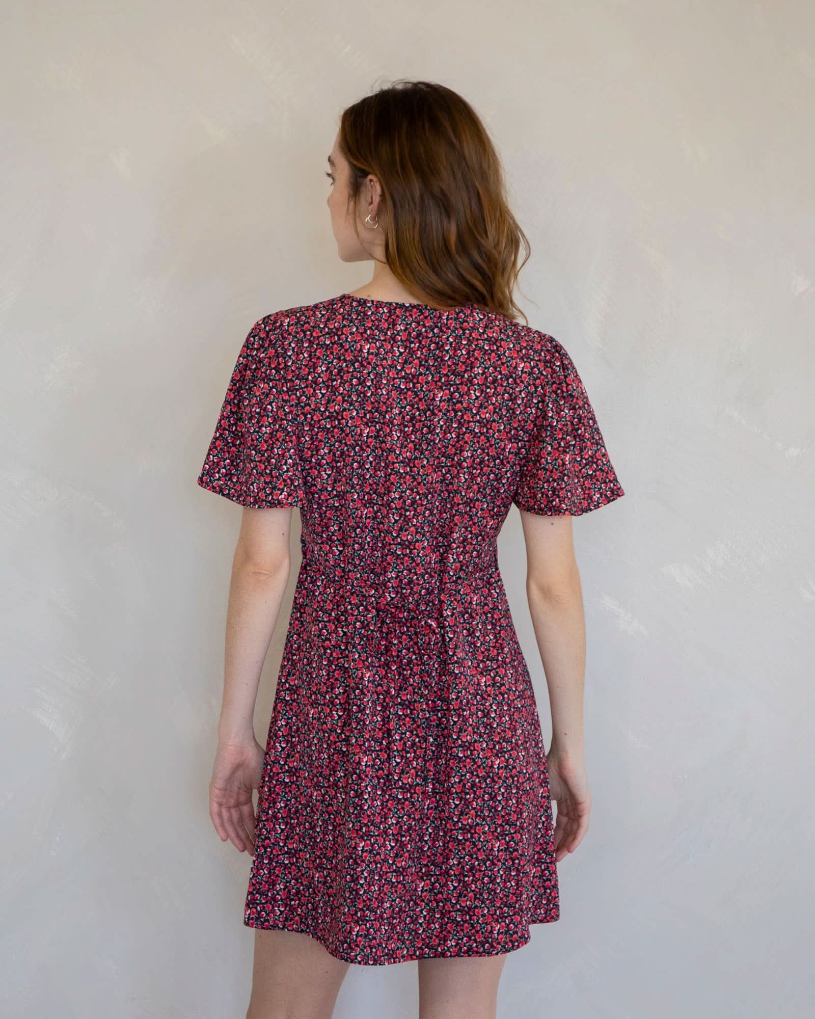 Woman wearing a red floral dress against a white wall