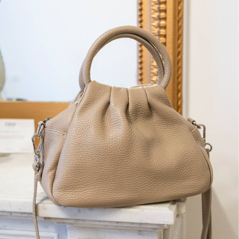 Beige handbag on a decorative white surface with a gold-framed mirror in the background