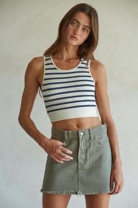 Woman wearing a white and light blue striped sleeveless U-V neckline tank top with a green mini skirt.