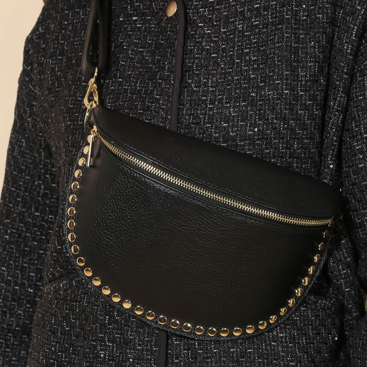Black waist bag with gold studs worn by a person in a textured black outfit.