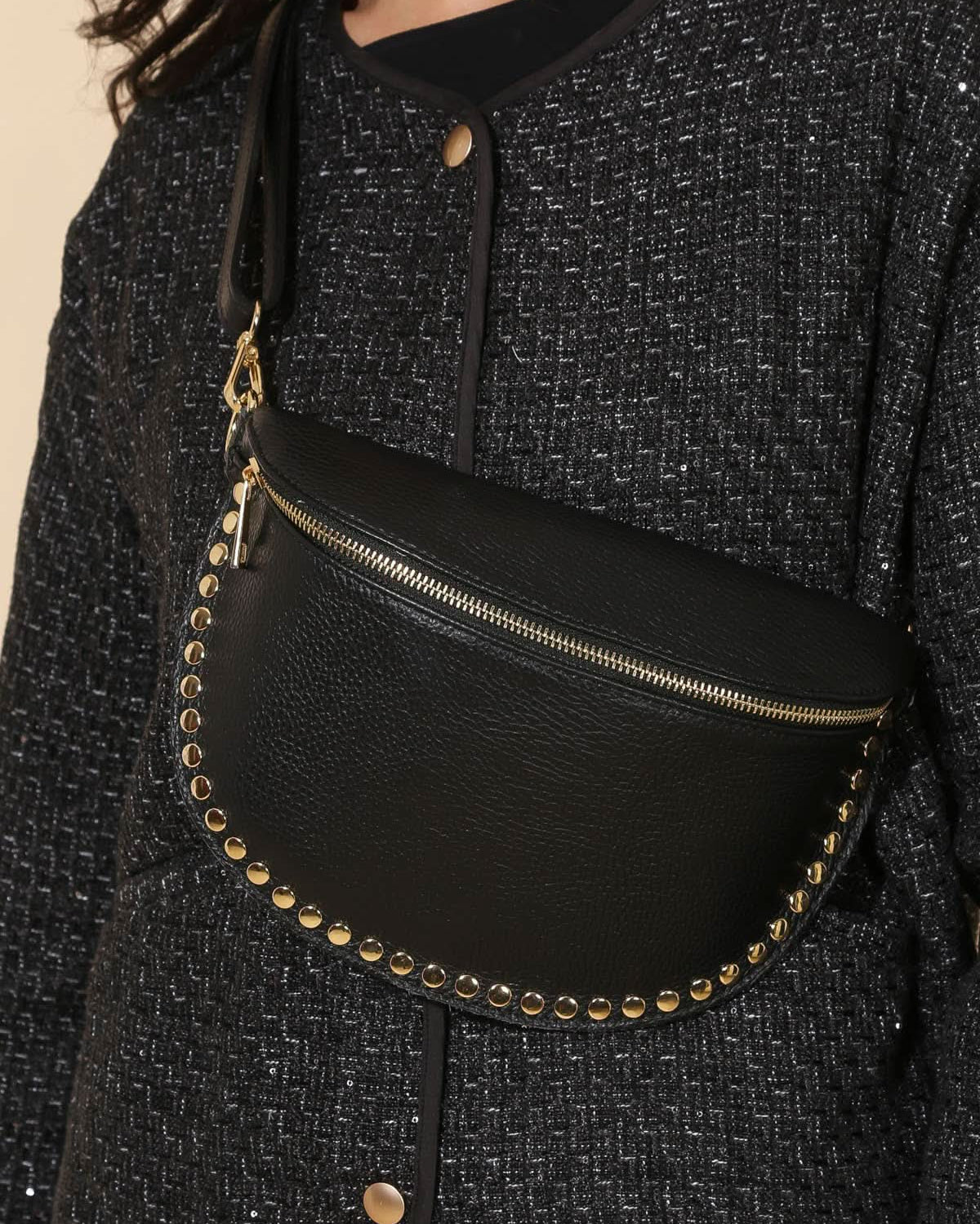 Black waist bag with gold studs worn by a person in a textured black outfit.