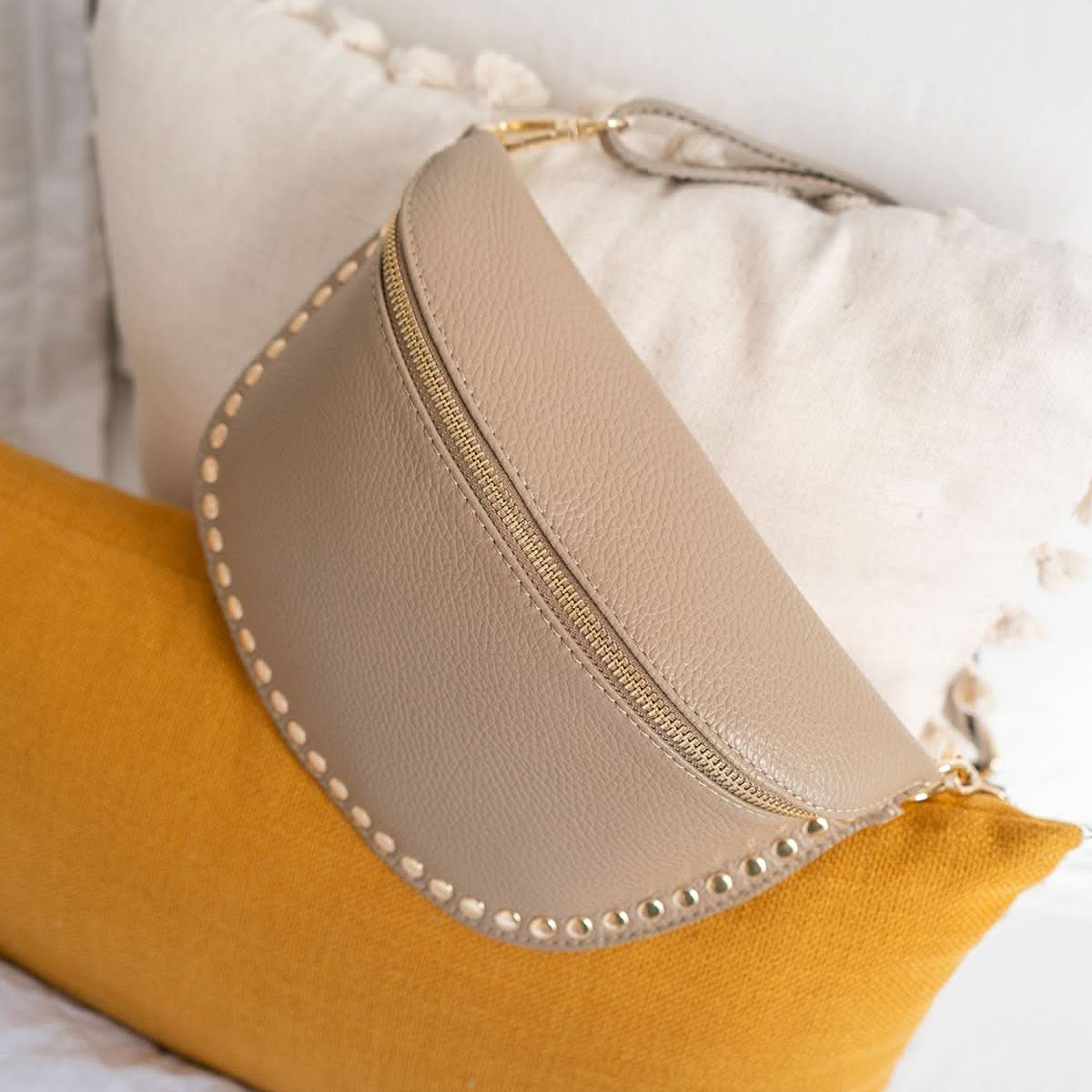 Beige pouch with decorative studs on a yellow pillow against a white background