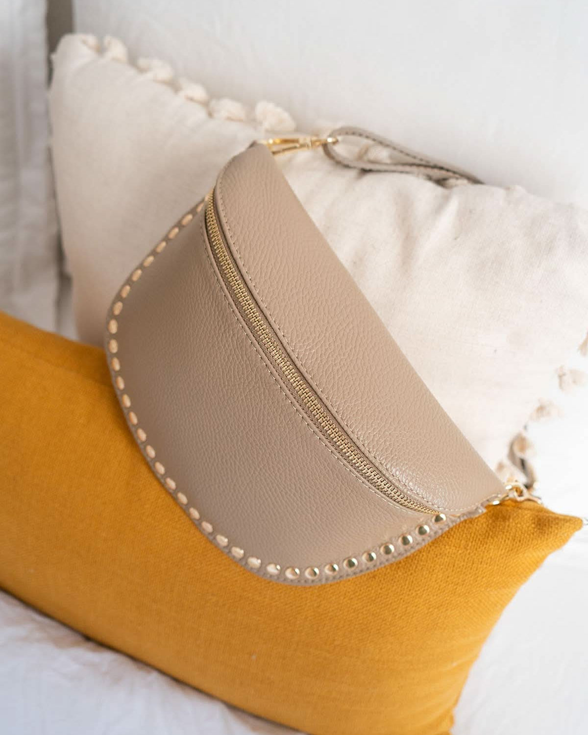 Beige pouch with decorative studs on a yellow pillow against a white background