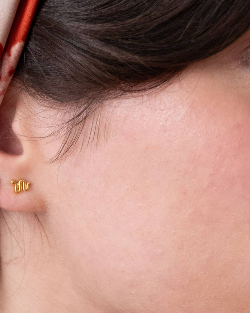 Close-up of a person wearing gold earrings with a red and white patterned fabric in the background