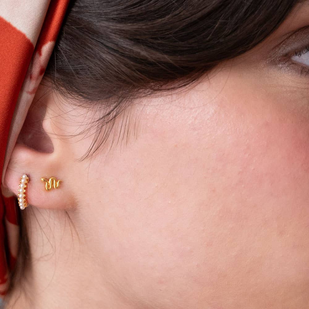 Close-up of a person wearing gold earrings with a red and white patterned fabric in the background