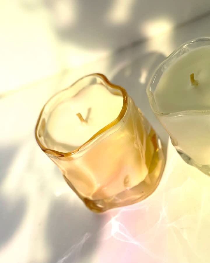 Two candles in wavy glass containers, one tinted pink the other clear glass