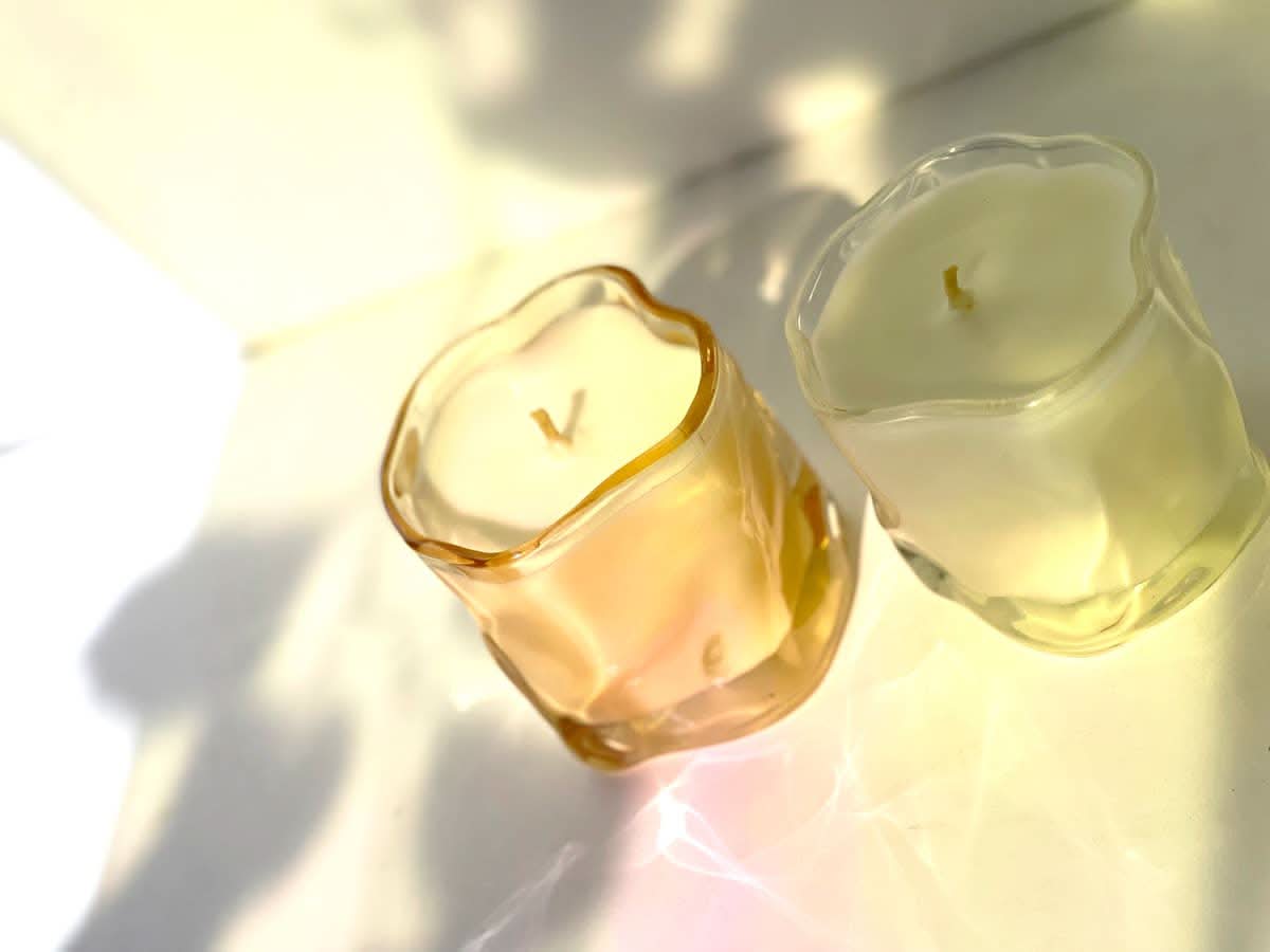 Two candles in wavy glass containers, one tinted pink the other clear glass
