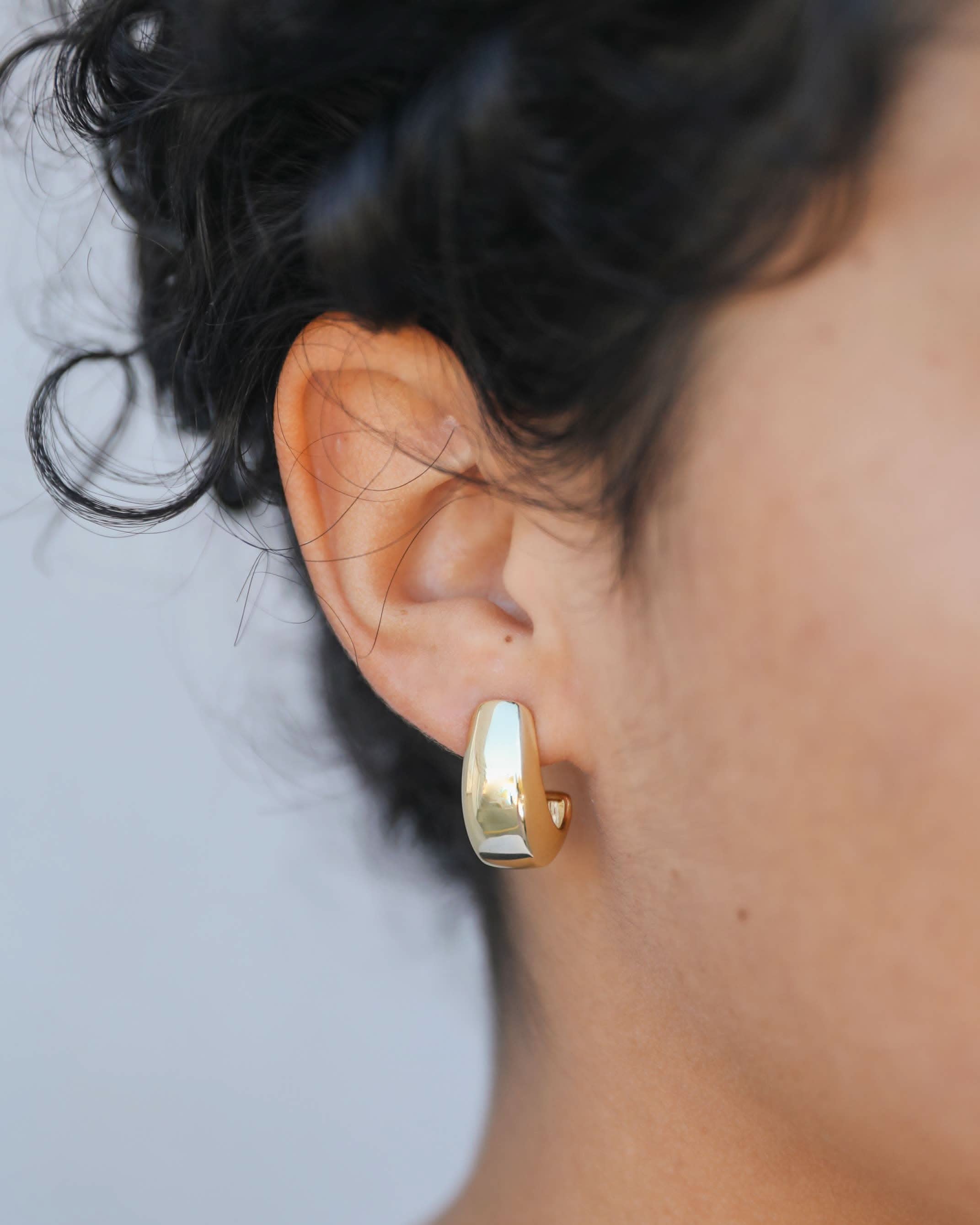 Close-up of a person wearing a gold hoop earring with a blurred background