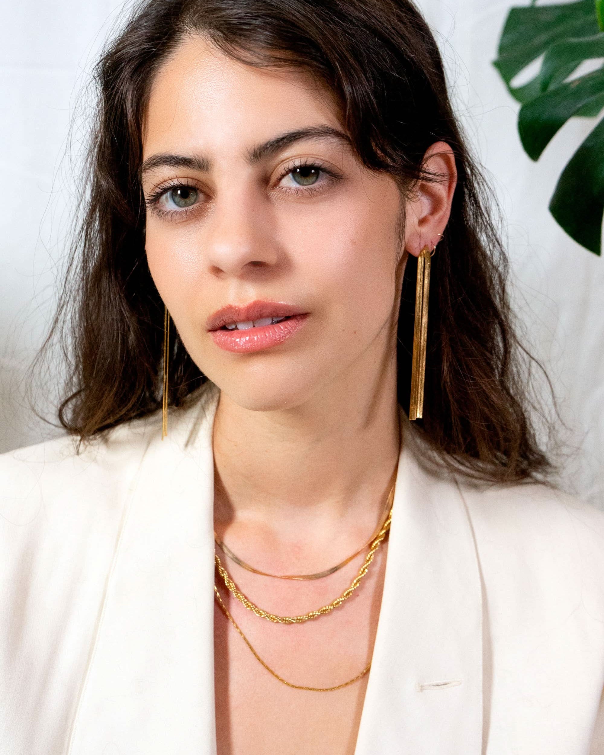 Woman wearing gold earrings and necklaces against a white background