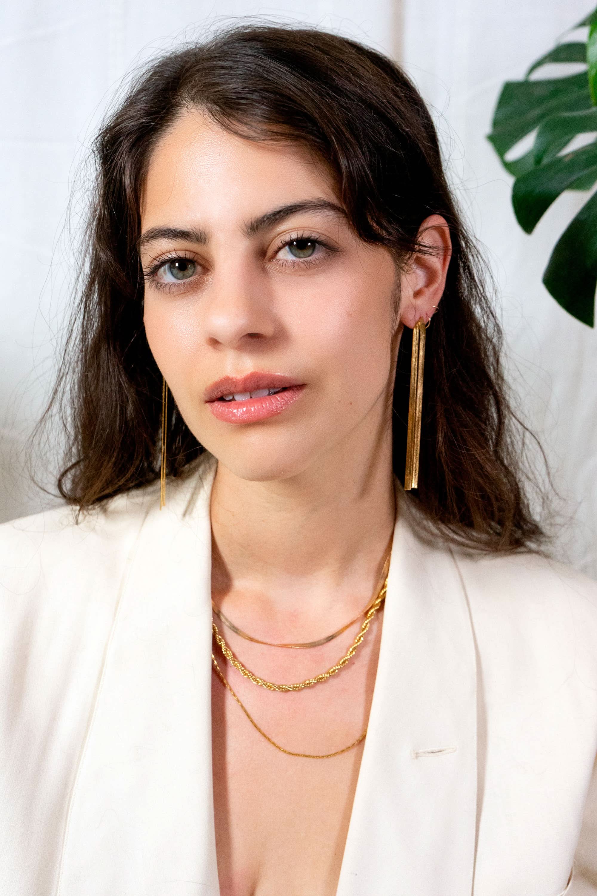 Woman wearing gold earrings and necklaces against a white background