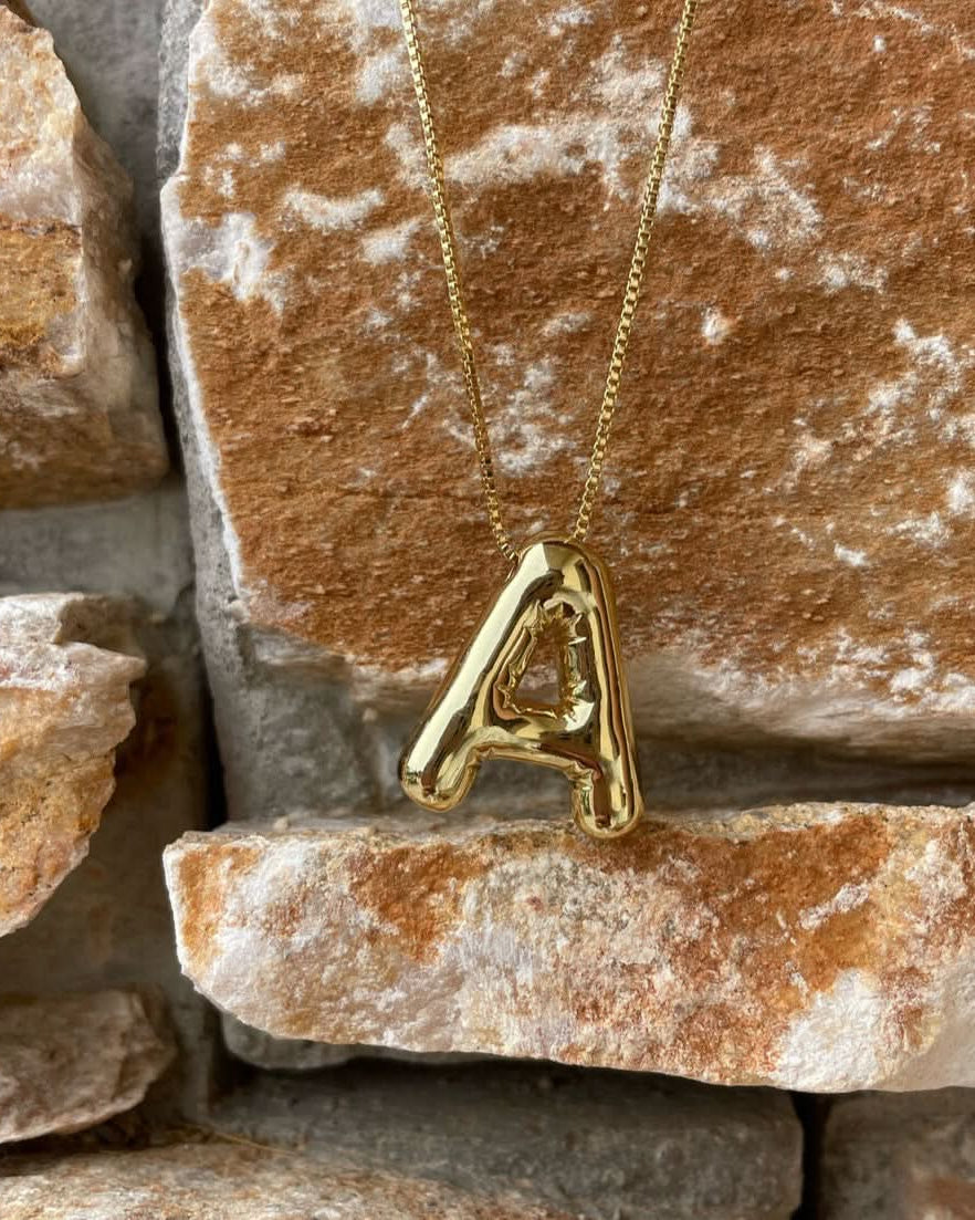 Gold necklace with a 'A' pendant on a stone background