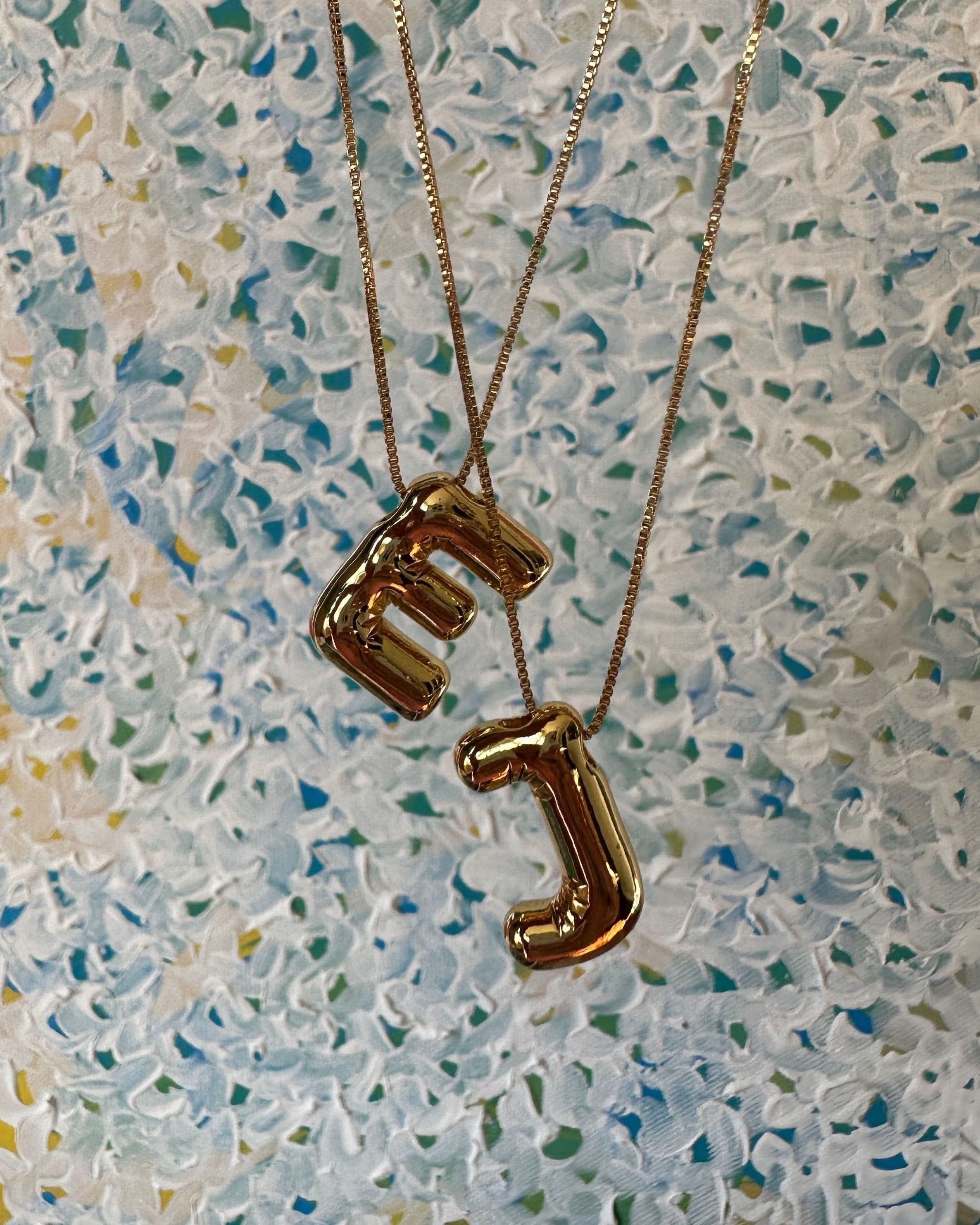 Gold necklaces with letter E & J pendants on a textured surface